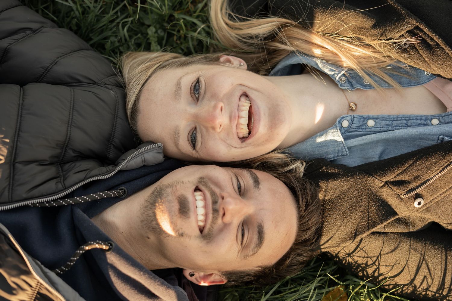 Two people laying on grass together smiling during an outdoor autumn photoshoot.