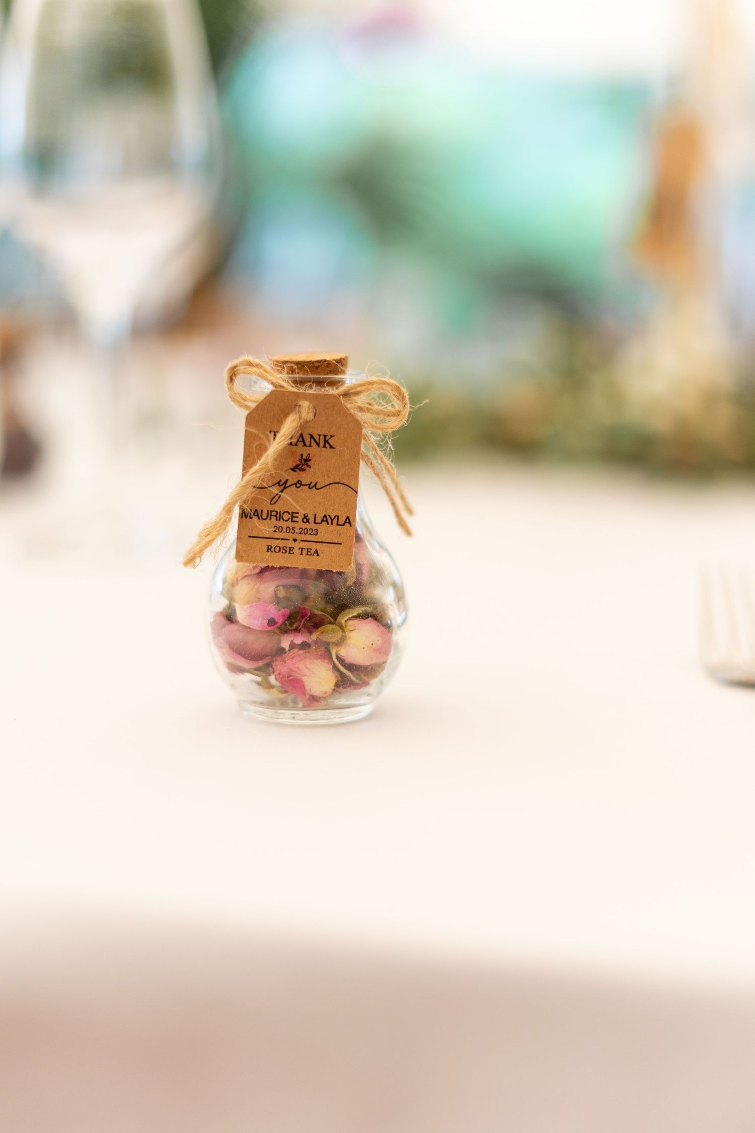 Small glass jar with a rustic twine bow containing colorful decorative items on a white surface.