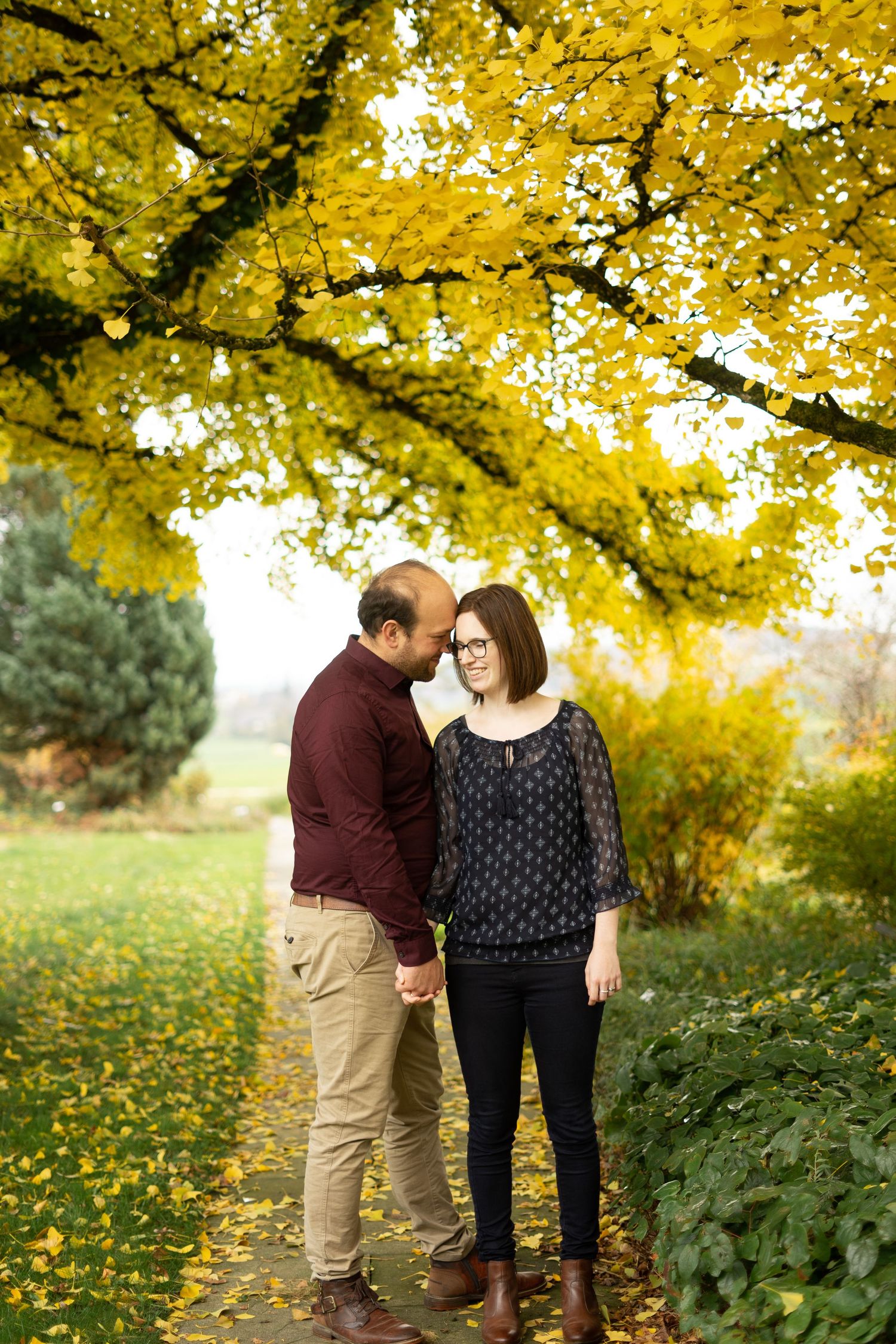 A couple stands intimately beneath vibrant yellow fall foliage in an autumn garden setting.