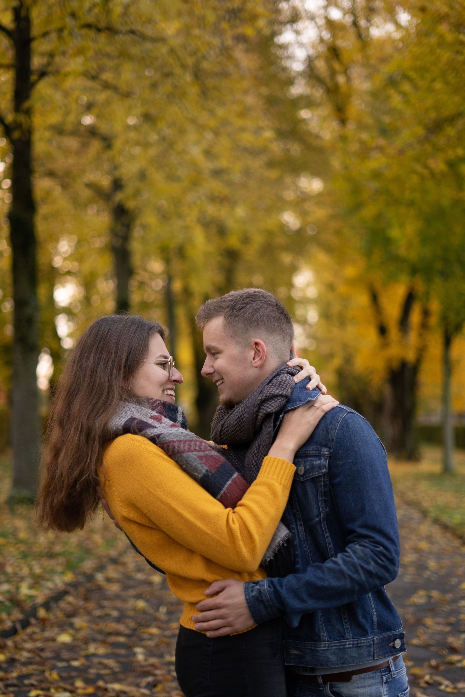 Couple sharing intimate moment surrounded by autumn trees with yellow leaves.