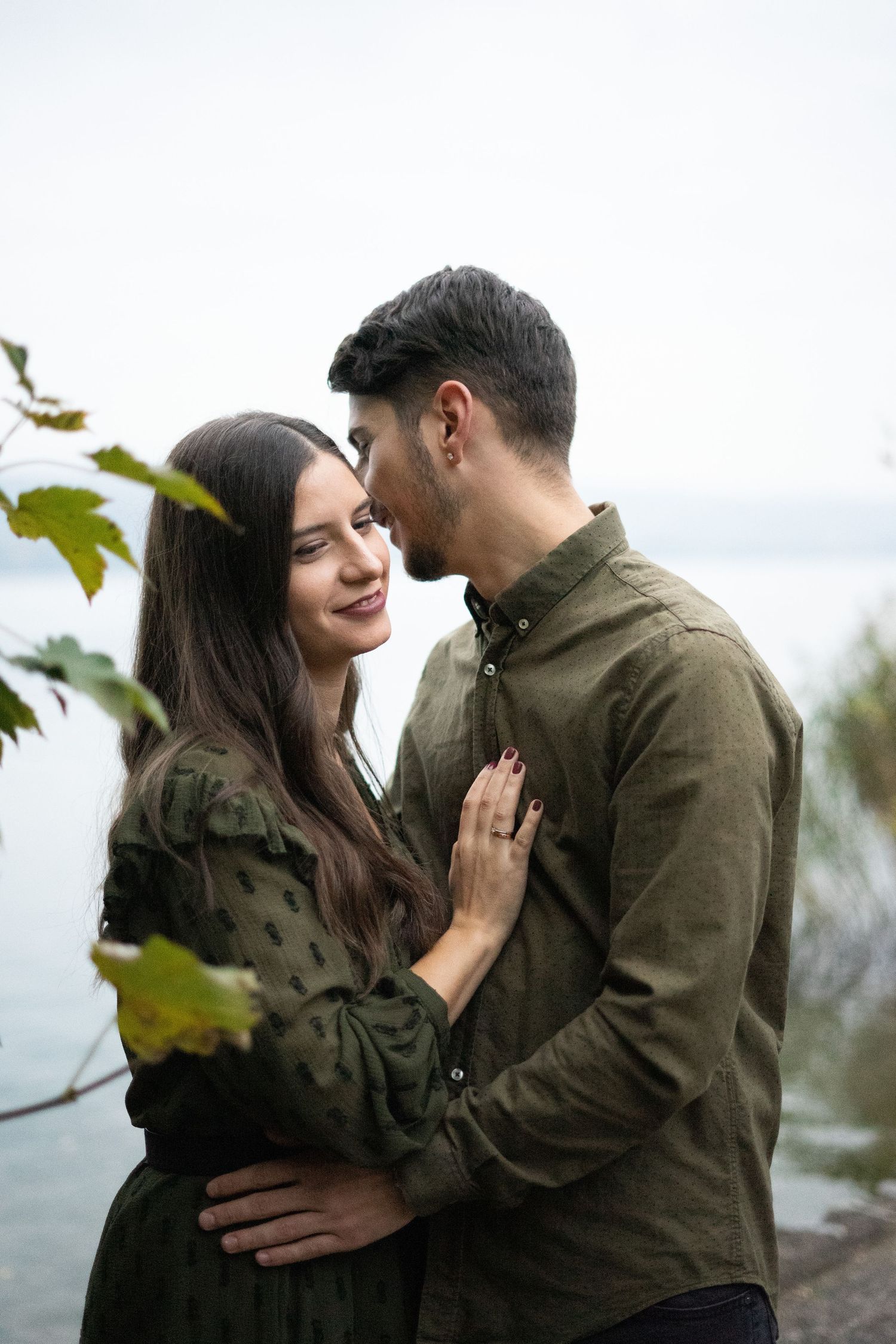 Couple in olive and black outfits sharing romantic moments outdoors.