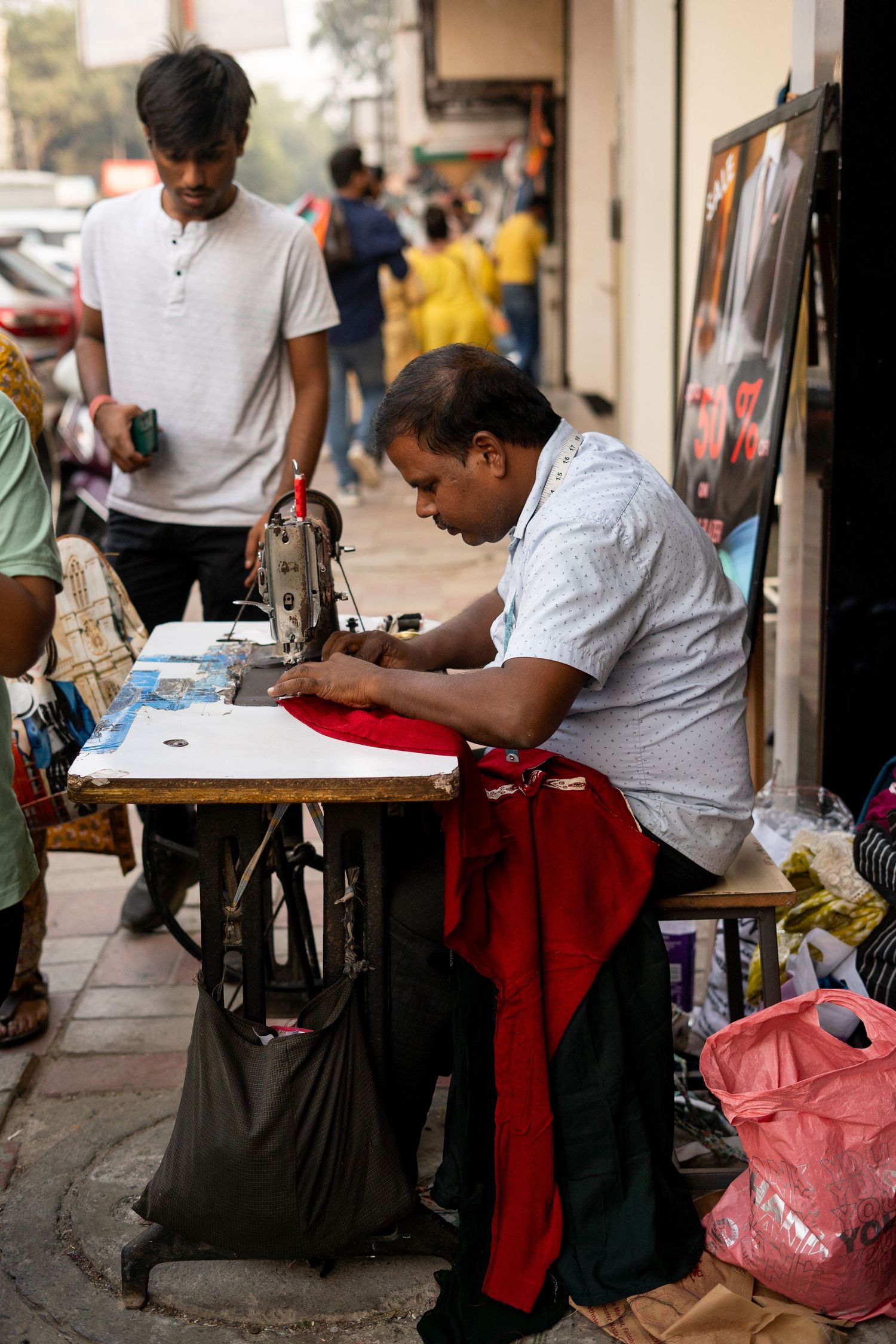 Street vendors sit at small tables on a busy sidewalk preparing traditional art and crafts.