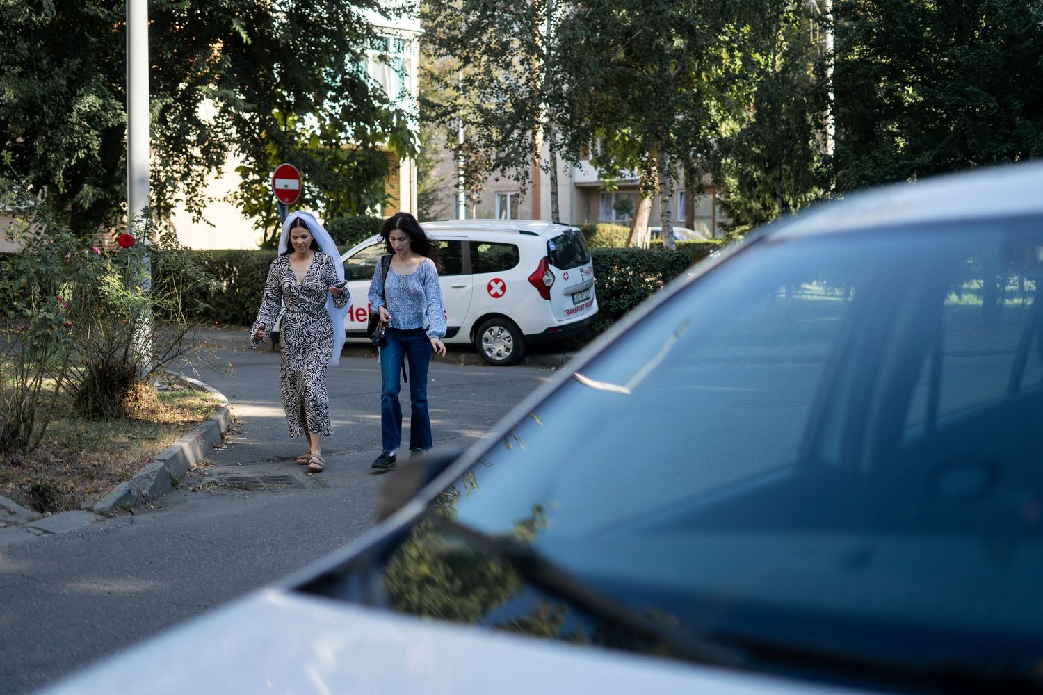 People walking through a parking lot on a sunny day with trees in the background.