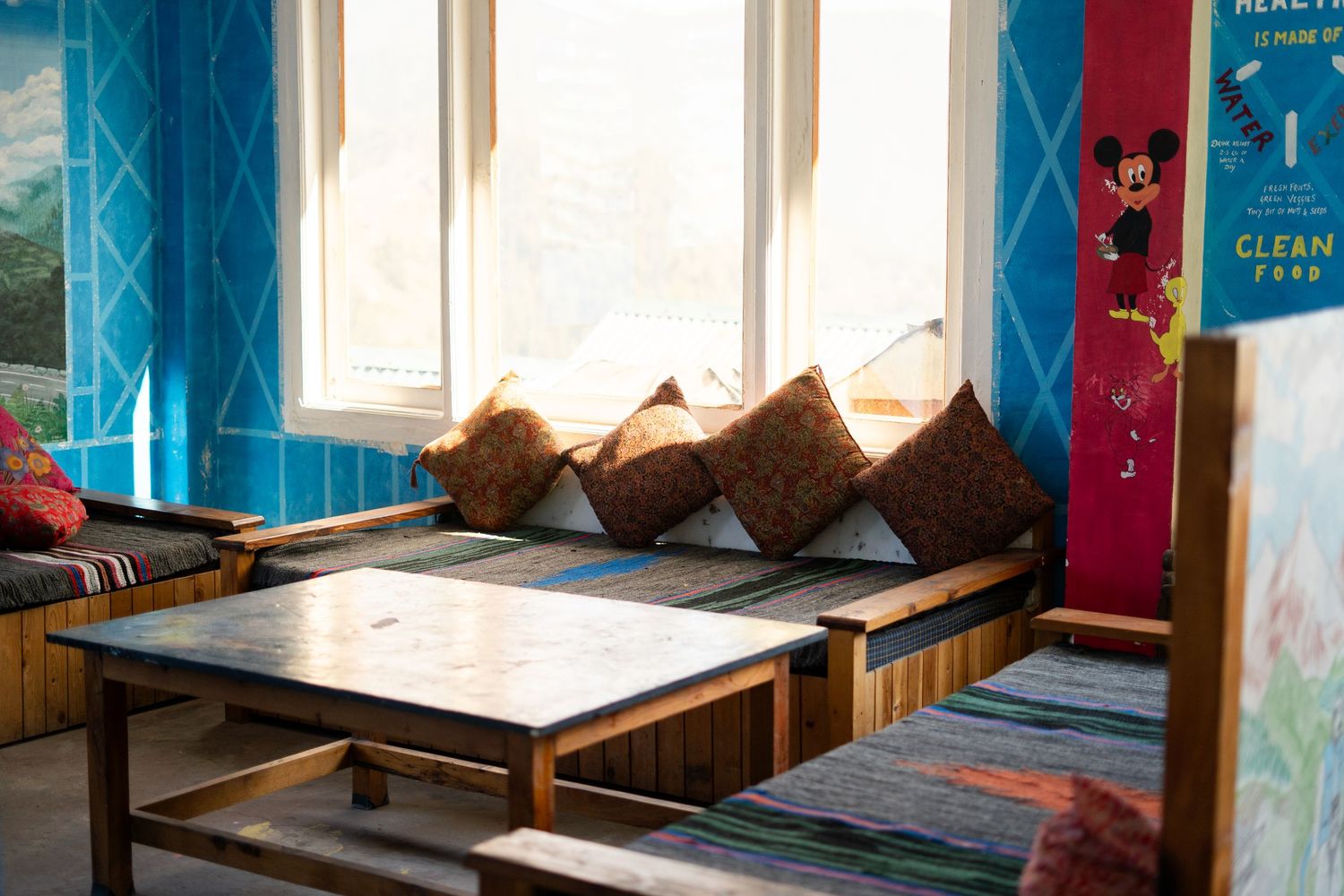 Cozy hostel interior with blue walls and wooden furniture by sunlit windows.