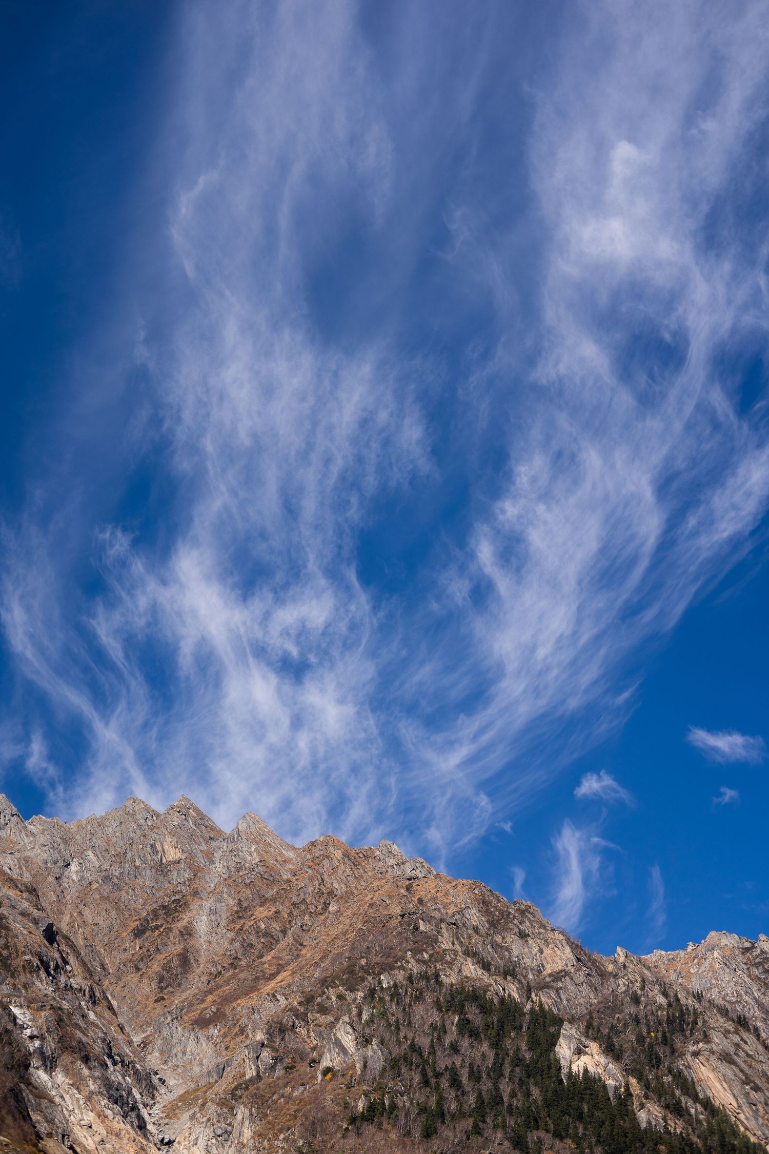 Dramatic rocky mountain peaks against a bright blue sky with wispy cirrus clouds.