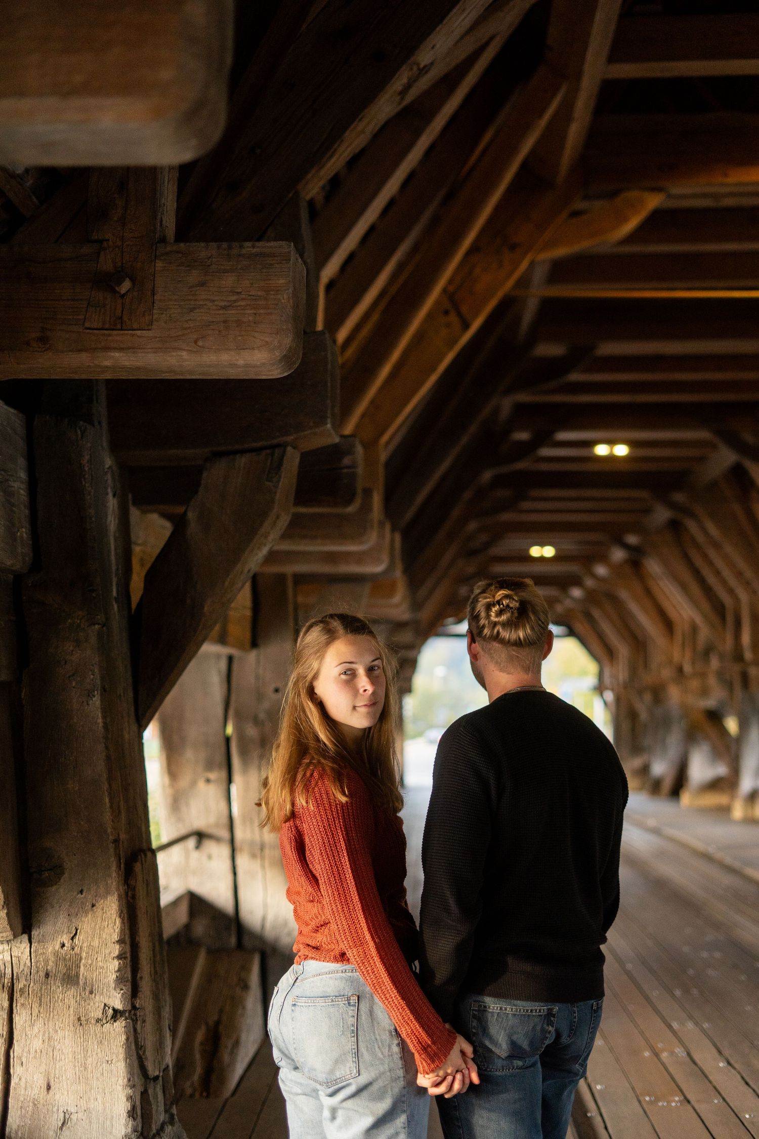 A couple holds hands while walking through a rustic wooden covered bridge.