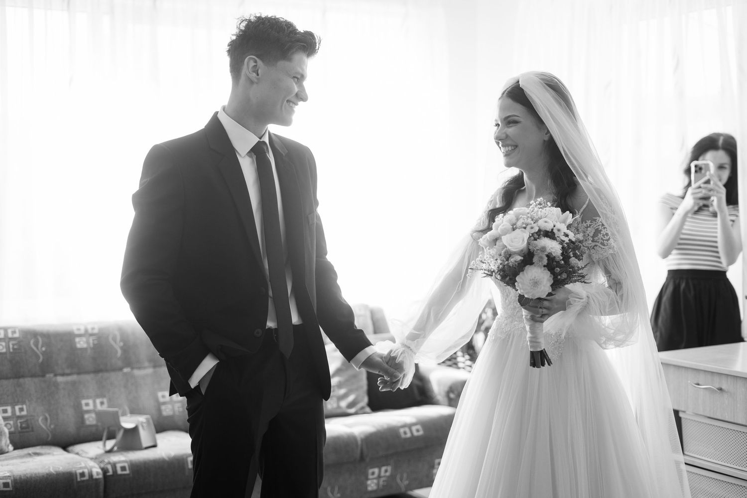 A bride and groom sharing a moment while someone takes photos in the background.
