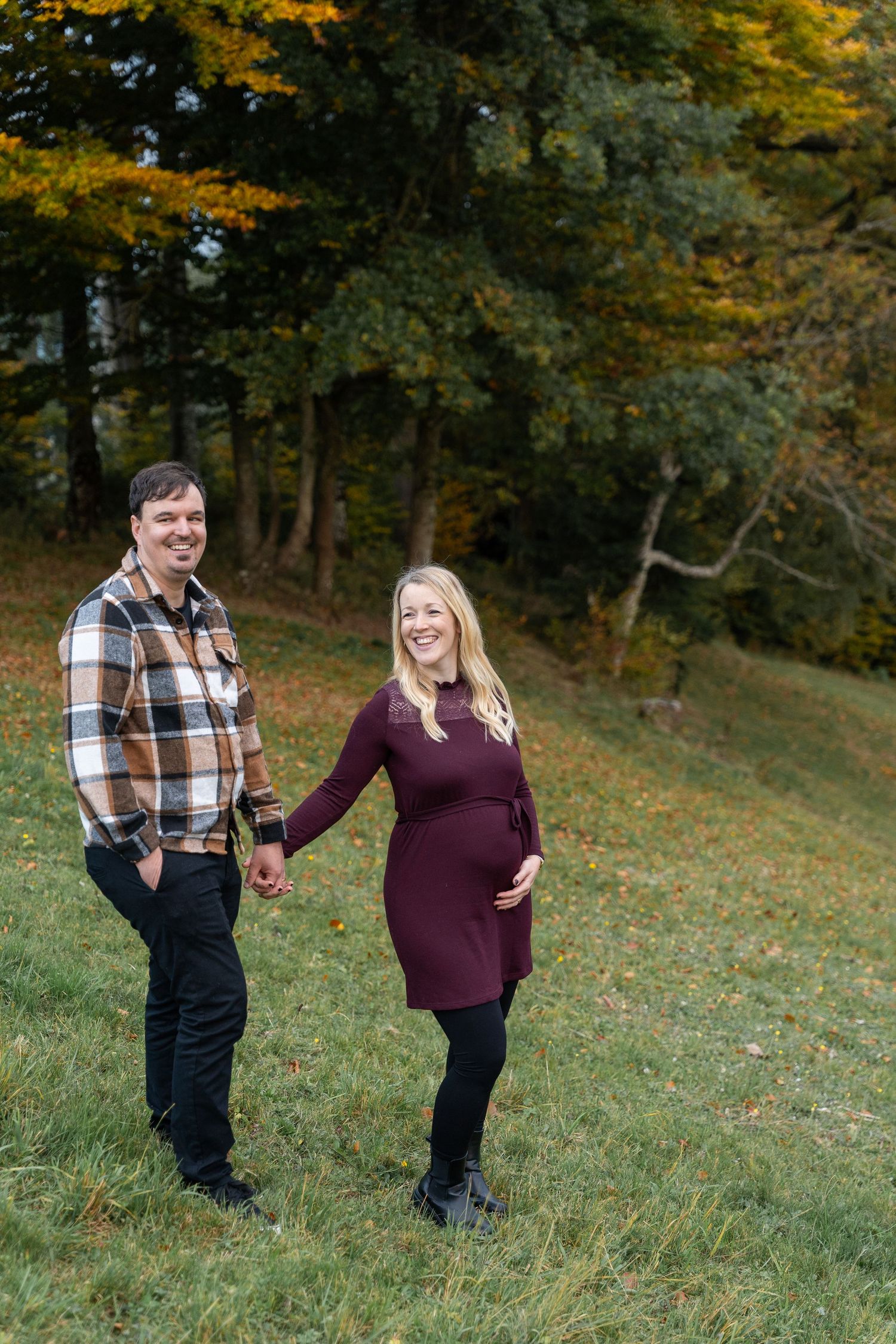 A couple shares a joyful moment together on a grassy hillside surrounded by autumn trees.