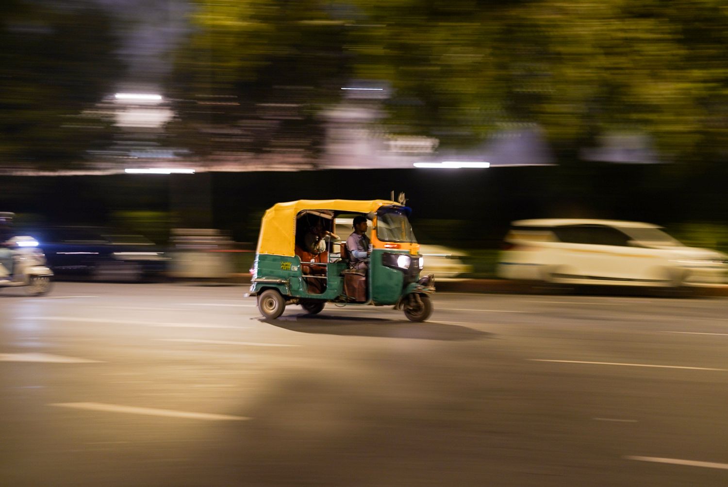 Motion-blurred vehicles passing on a street at dusk or night.