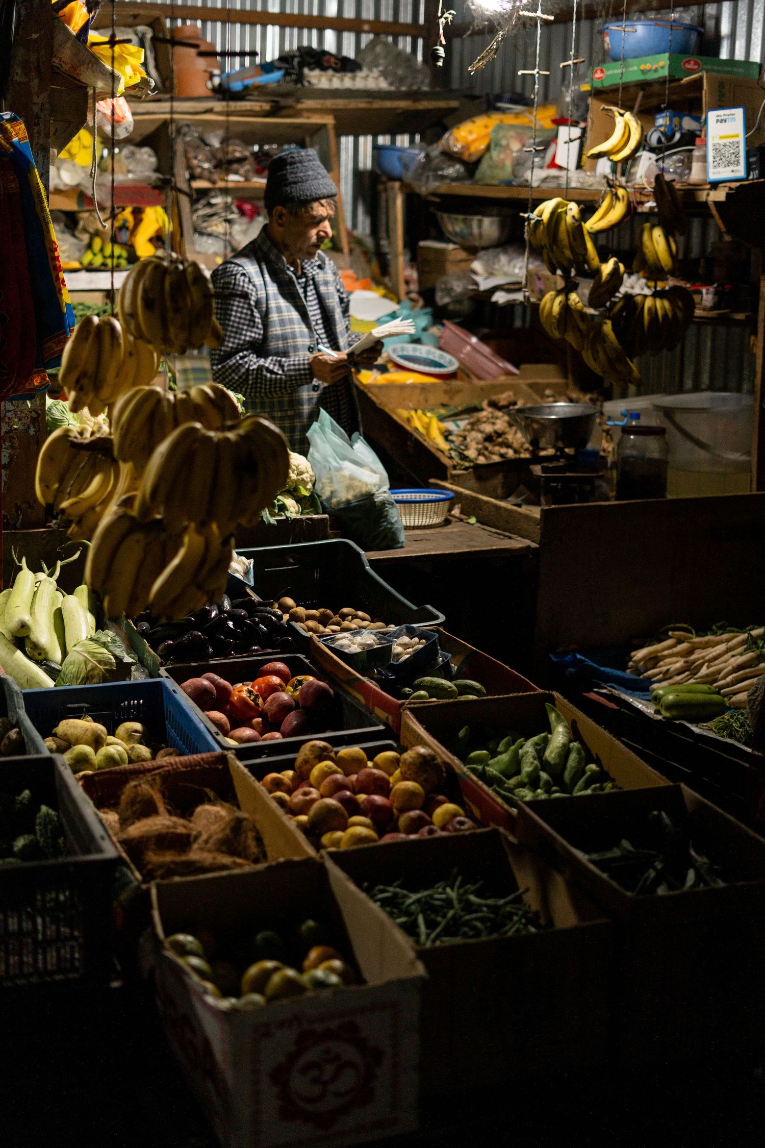Local market stall displaying fresh produce and bananas in wooden crates under dim lighting.