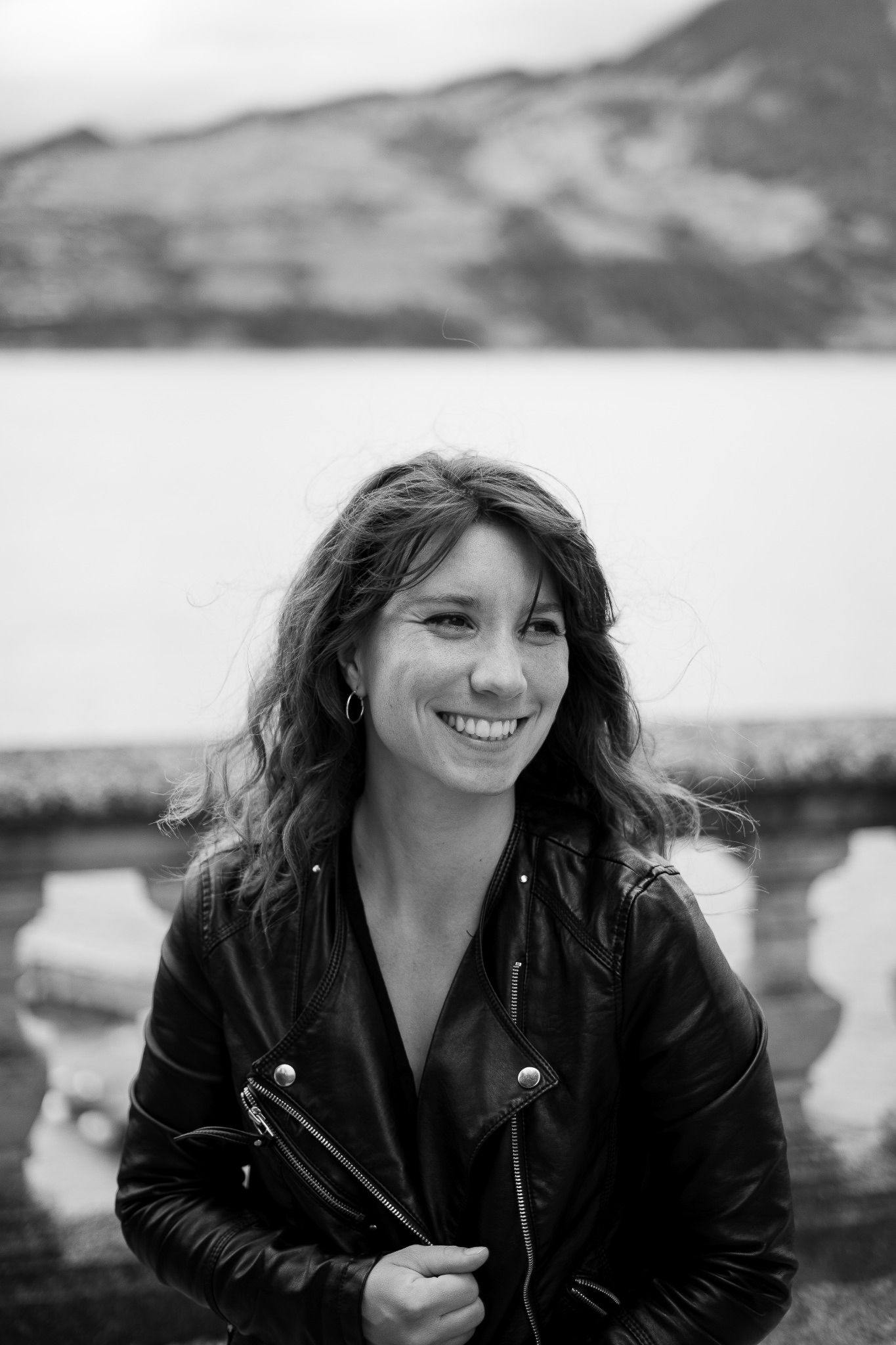 Black and white portrait of someone in leather jacket with mountains in background.