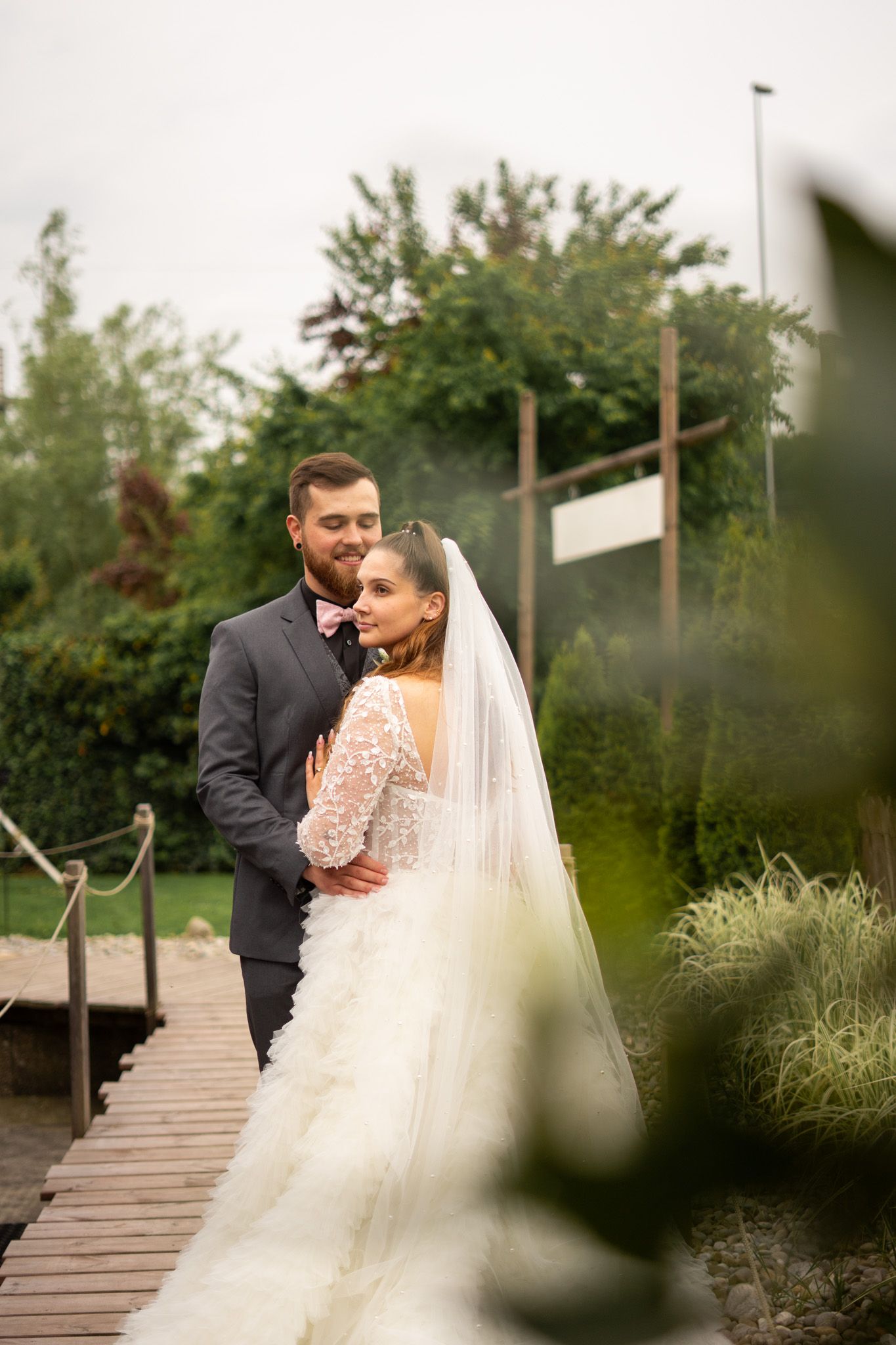 Couple shares romantic moments on wooden walkway surrounded by greenery.