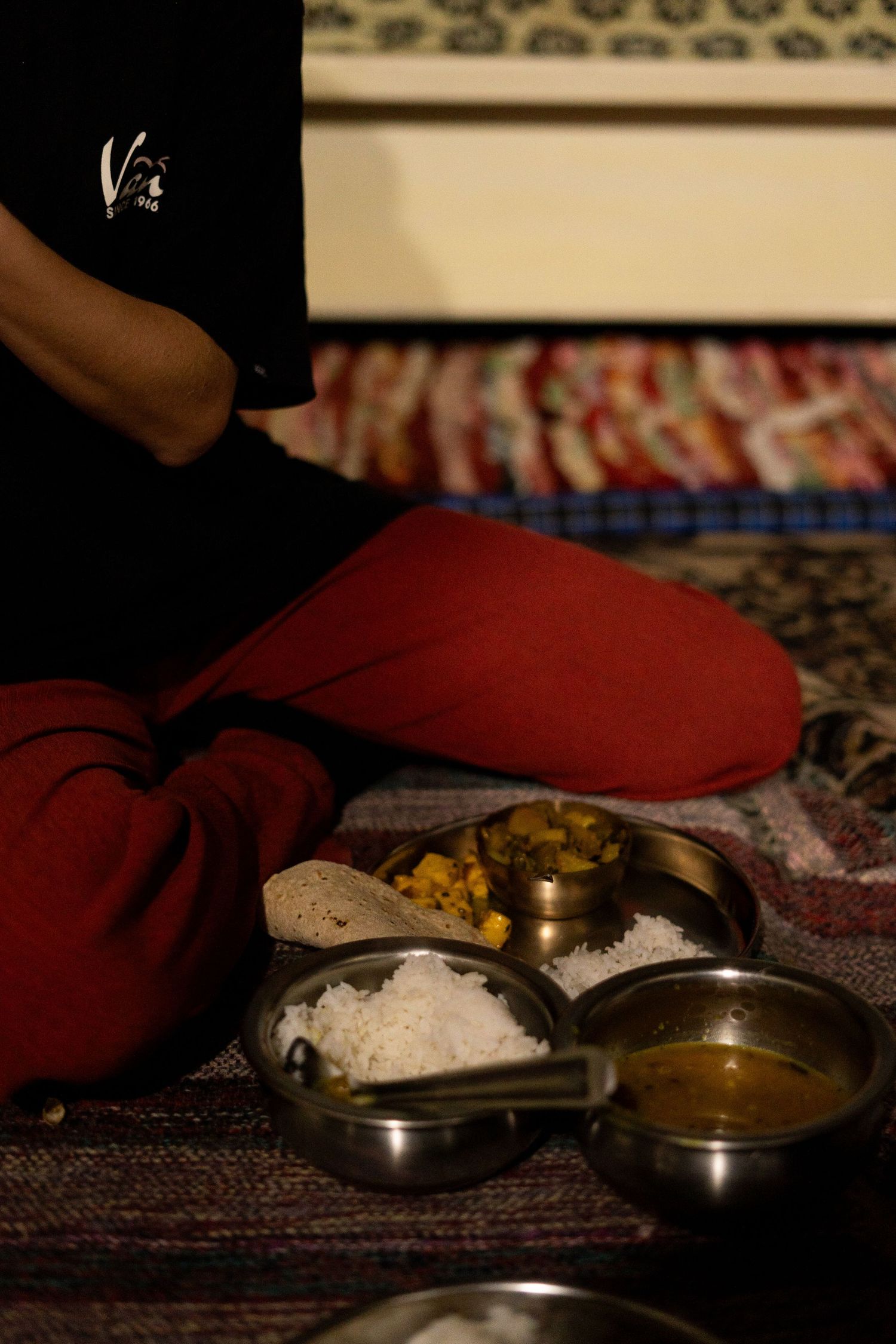 Traditional Indian meal setup with metal bowls containing various dishes on a patterned carpet.