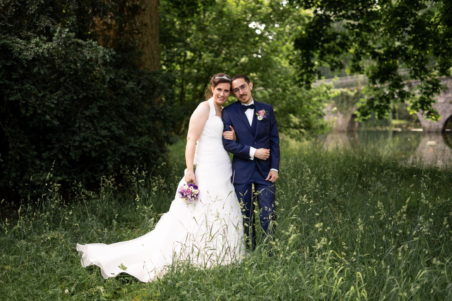 Romantic wedding couple poses in lush garden setting with natural greenery and summer lighting.