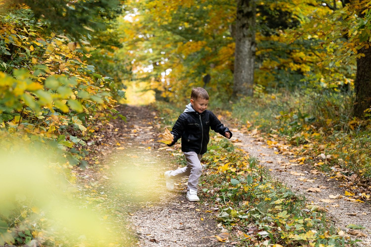 A small figure runs along a leaf-covered forest trail on an autumn day with golden foliage overhead.