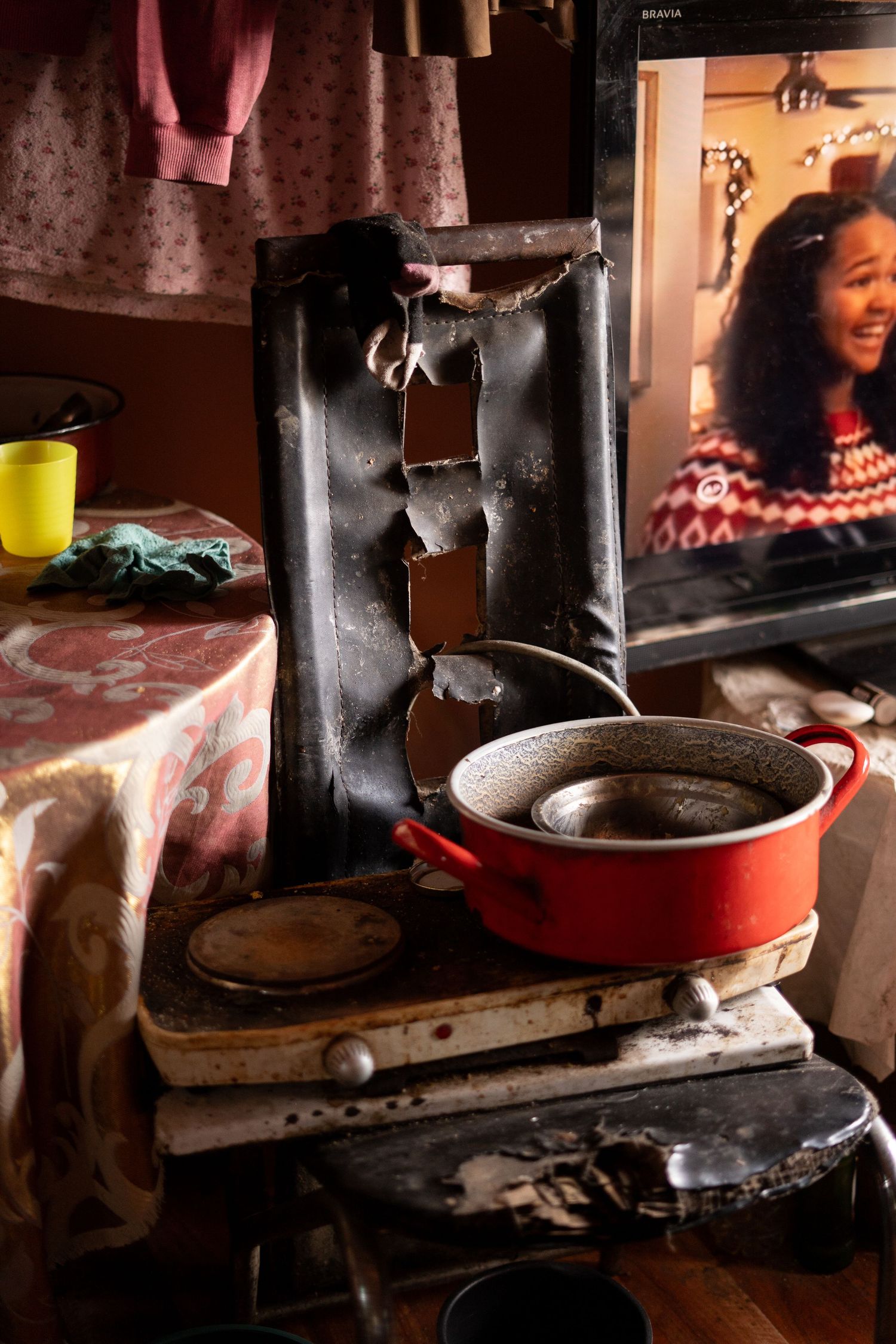 A rustic kitchen interior with a red pot on the stove and clothes hanging above.