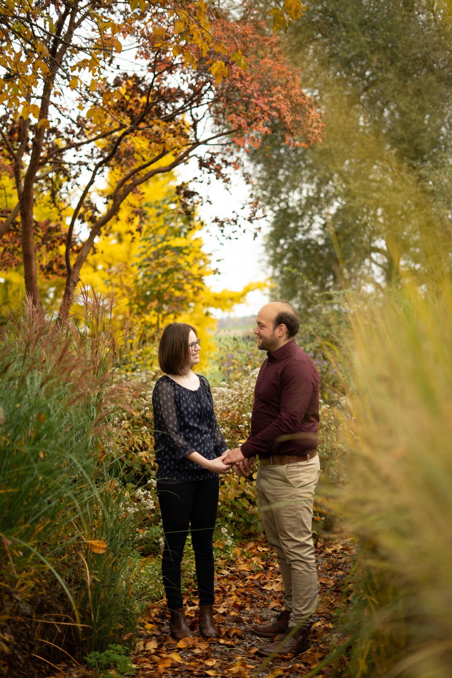A romantic autumn scene with a couple standing on a leaf-covered path surrounded by fall colors.