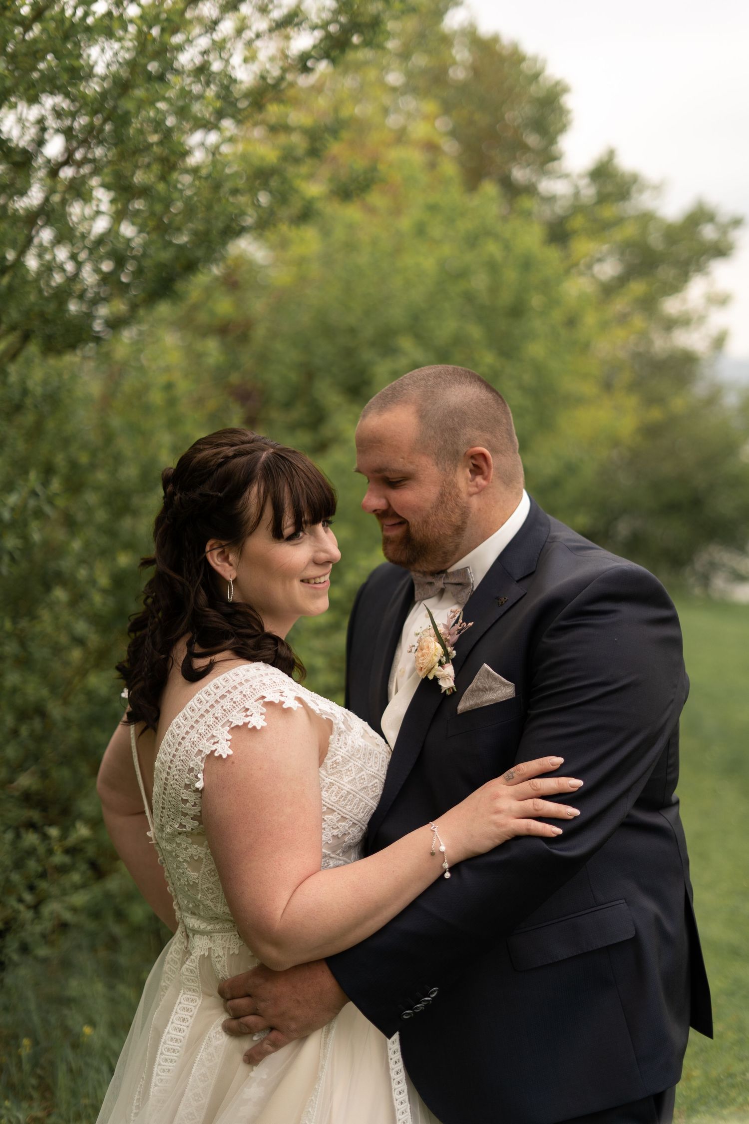 A romantic wedding portrait of a couple embracing outdoors surrounded by lush greenery.