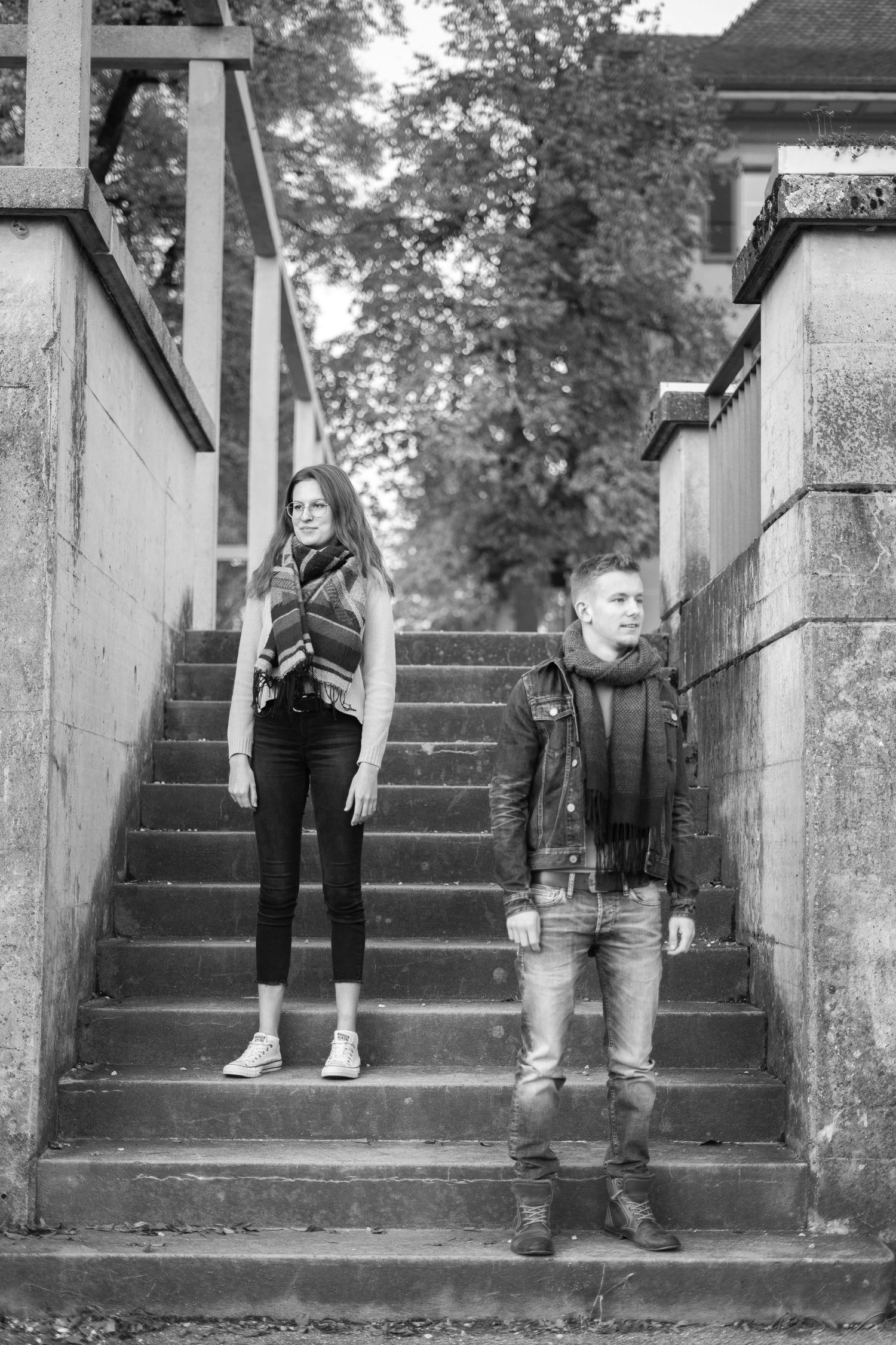A black and white portrait of a couple posed separately on concrete steps.