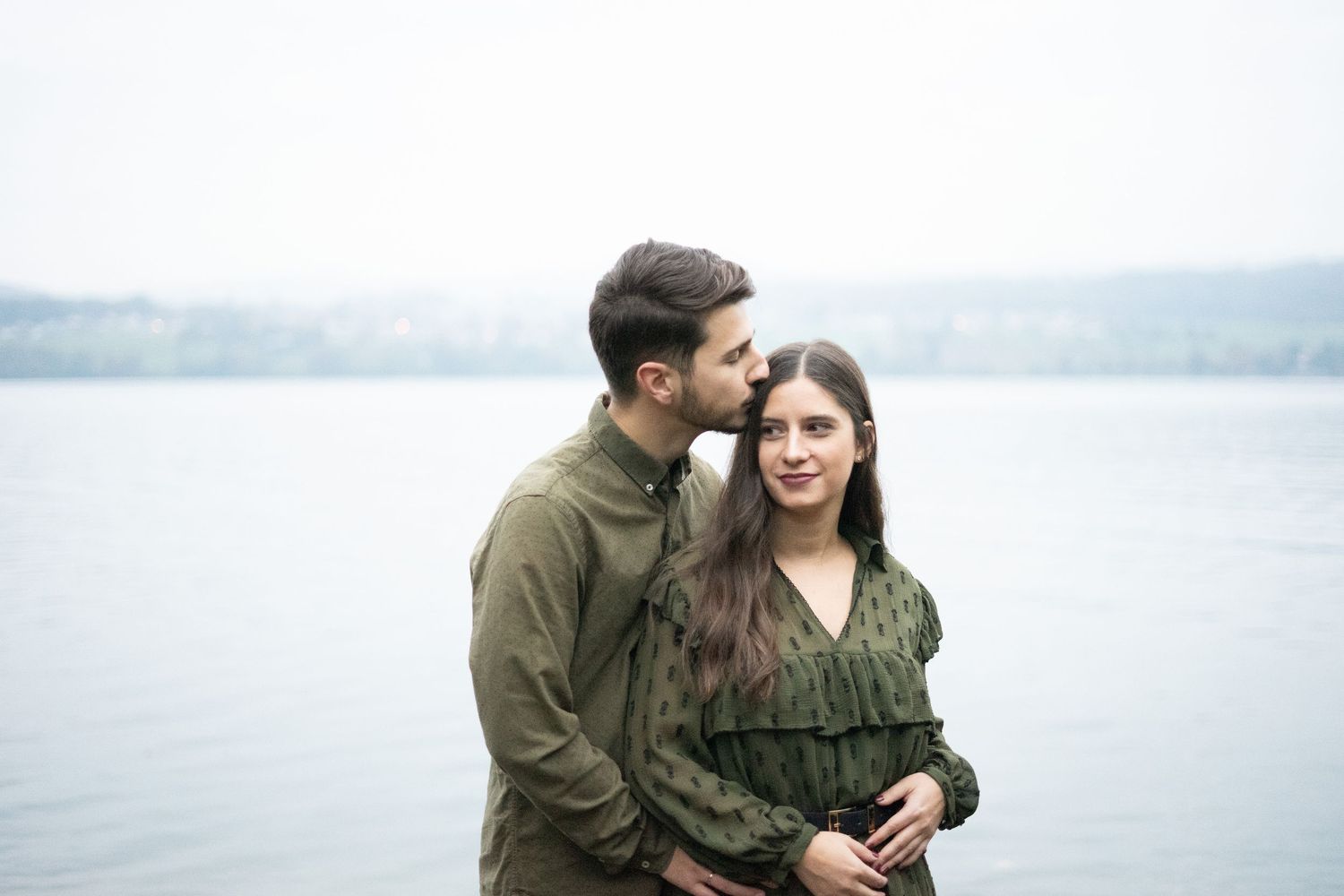 Couple sharing tender moments by a misty lake in casual winter wear.