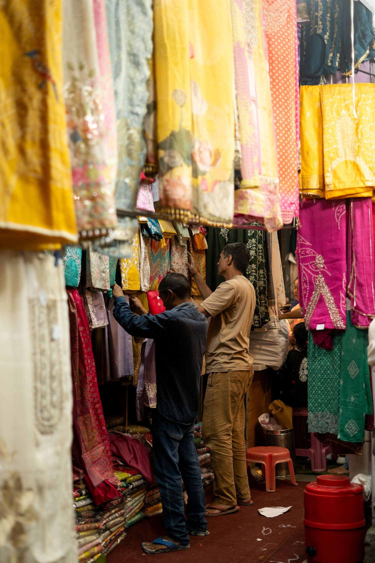 Vendors arranging vibrant fabrics and clothing at market stalls against yellow walls.