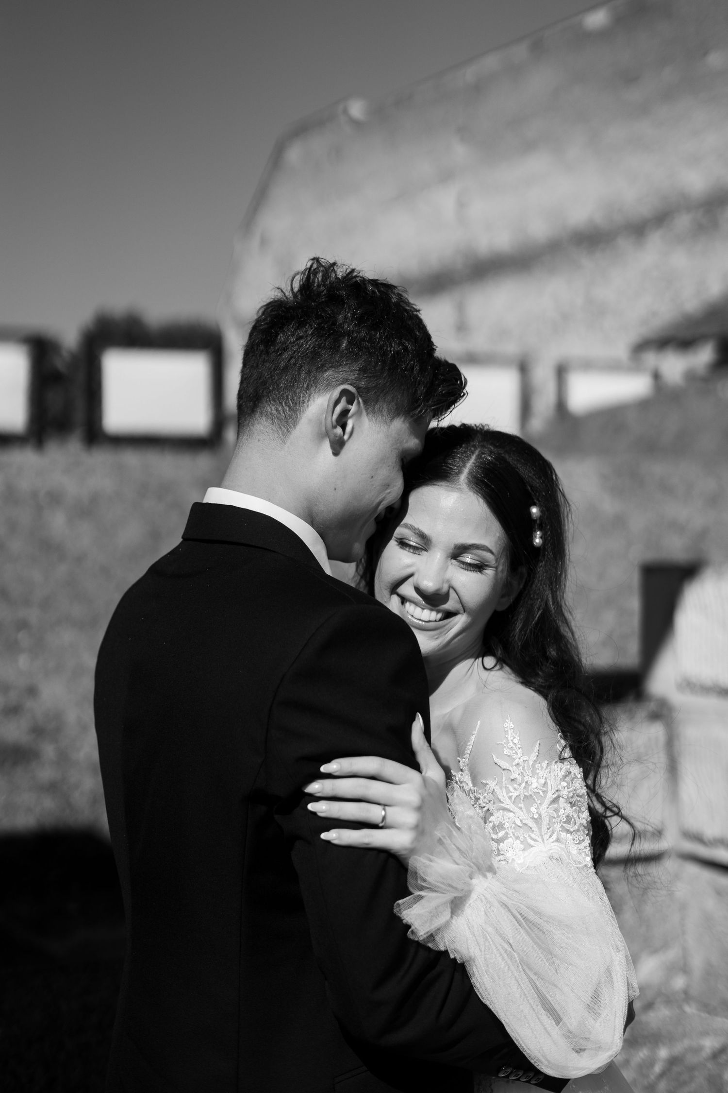 Wedding couple shares an intimate moment against a cloudy sky in black and white photography.