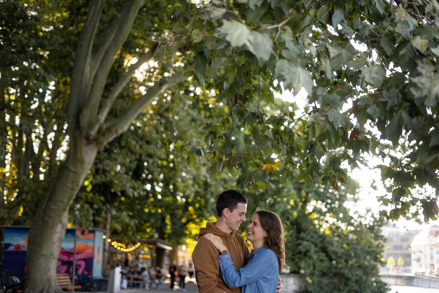 Romantic couple sharing a tender moment under green trees in an urban setting.