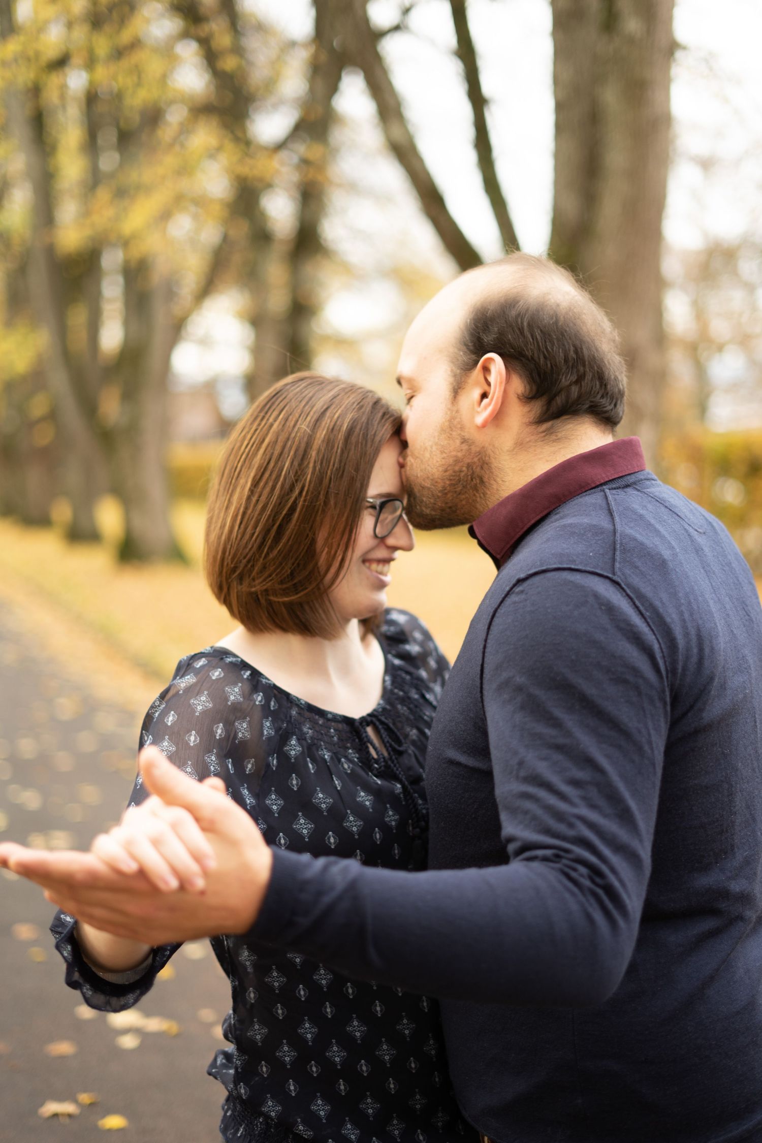 A couple dances together on a path covered in autumn leaves.