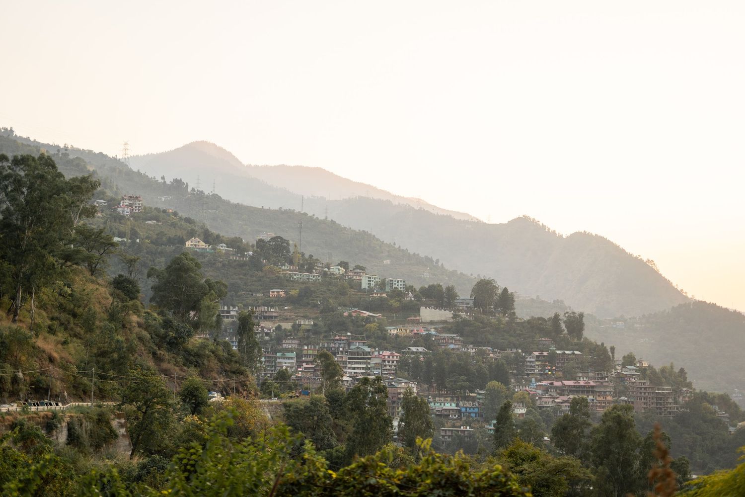 Mountain village nestled on hillside during sunset with hazy atmospheric conditions.