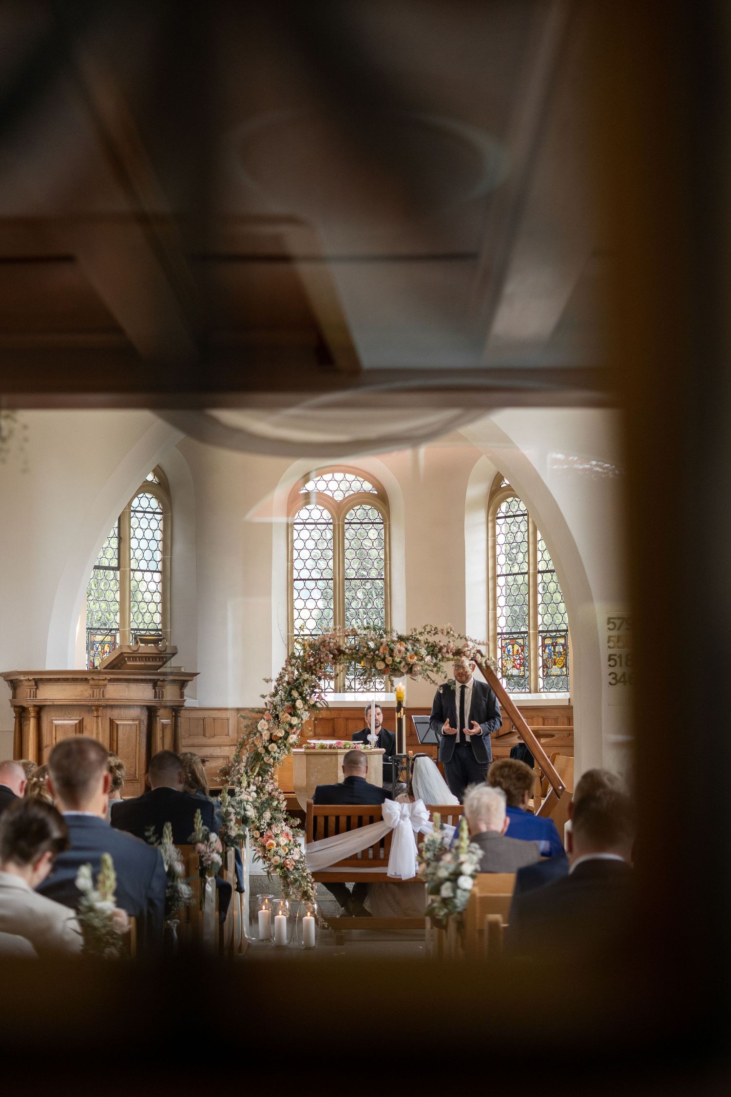 A wedding ceremony in a church with stained glass windows and floral arch decorations.