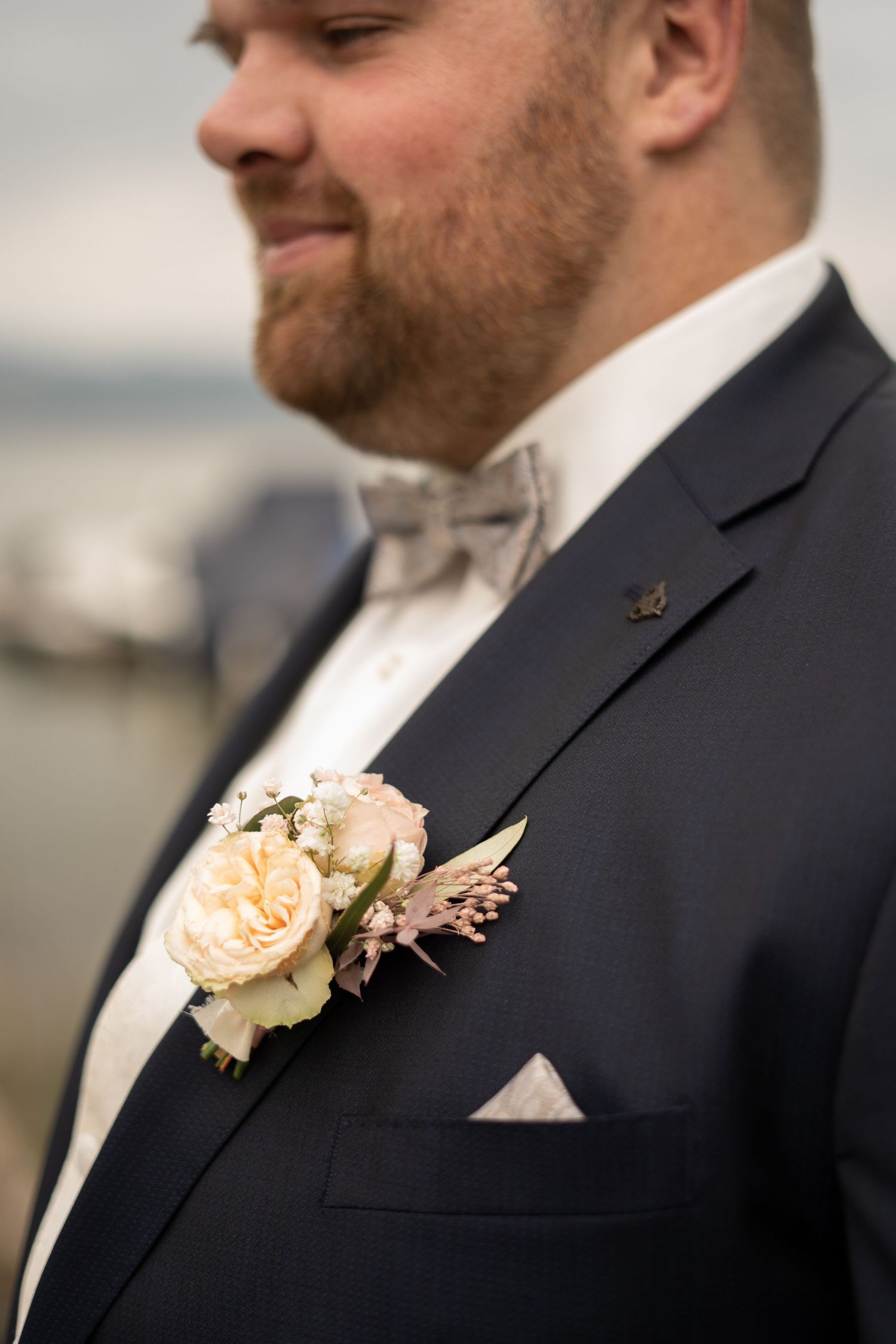 Close-up details of peach rose boutonniere on black suit jacket.