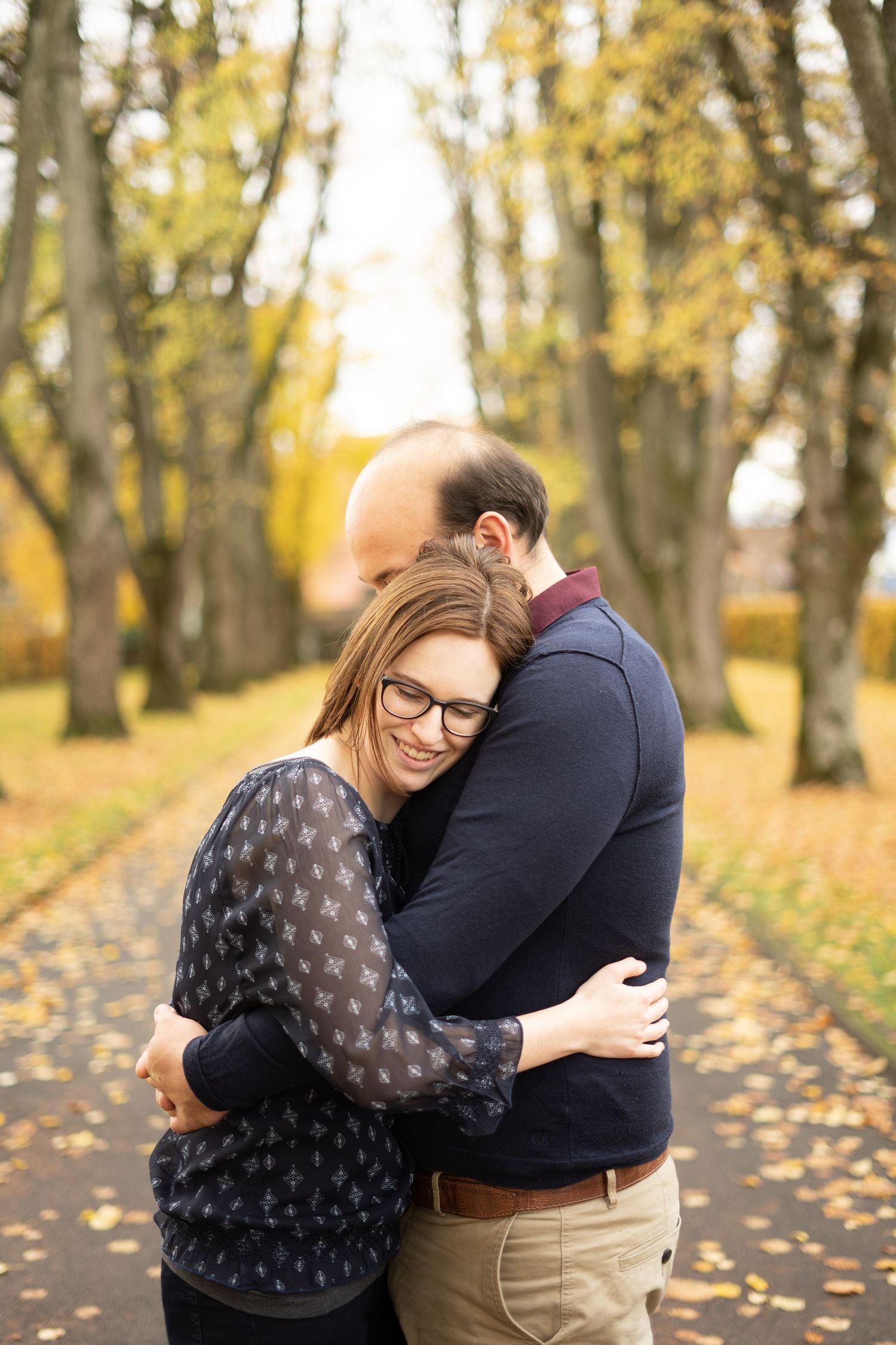 Couple embracing in autumn park with fallen leaves and golden trees.
