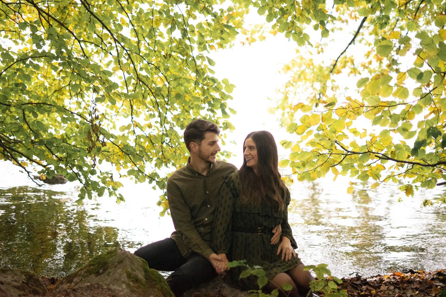 A romantic autumn photoshoot at the water's edge with golden sunlit trees overhead.