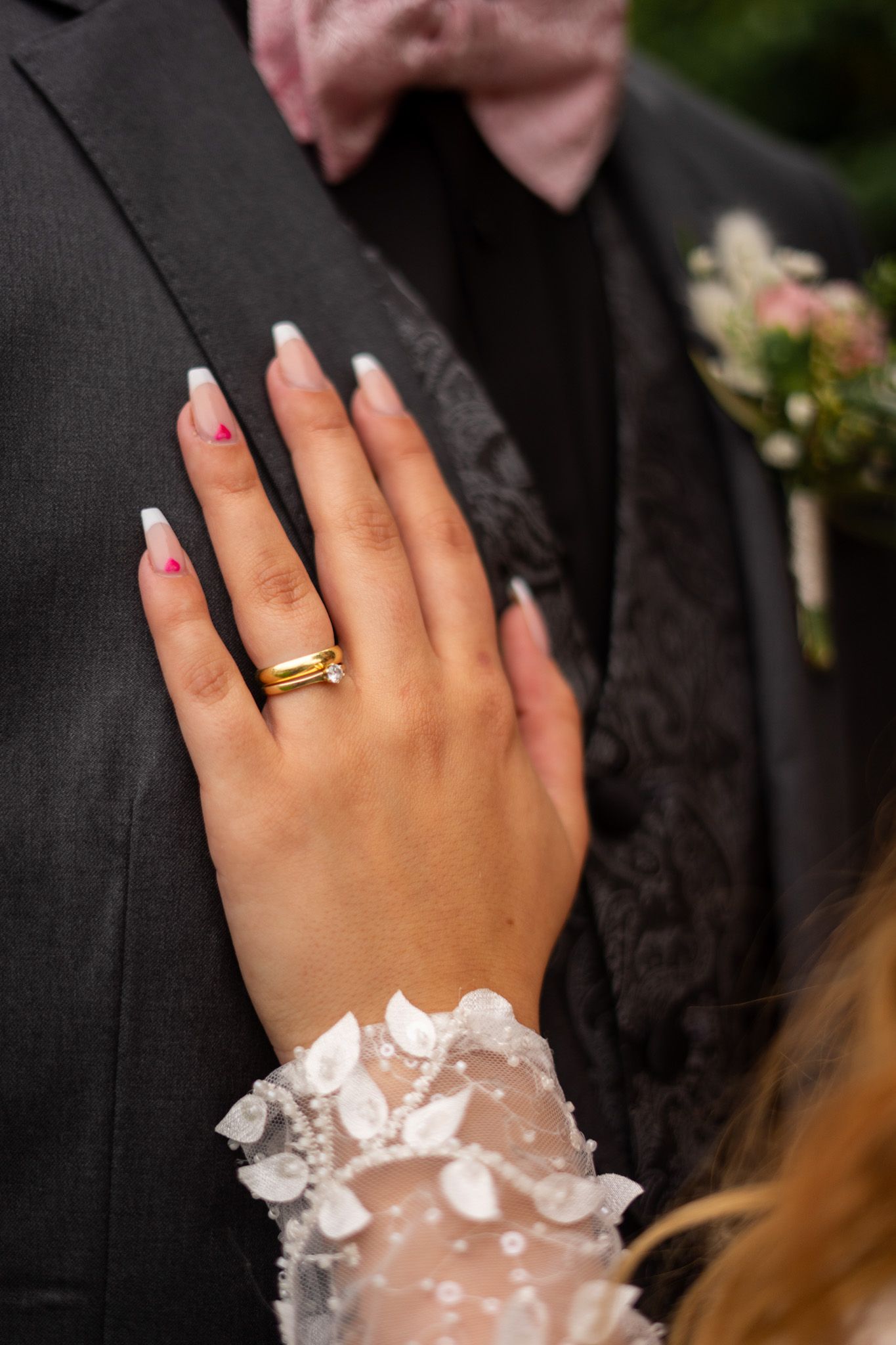 Close-up of wedding ring and delicate lace details on formal attire.
