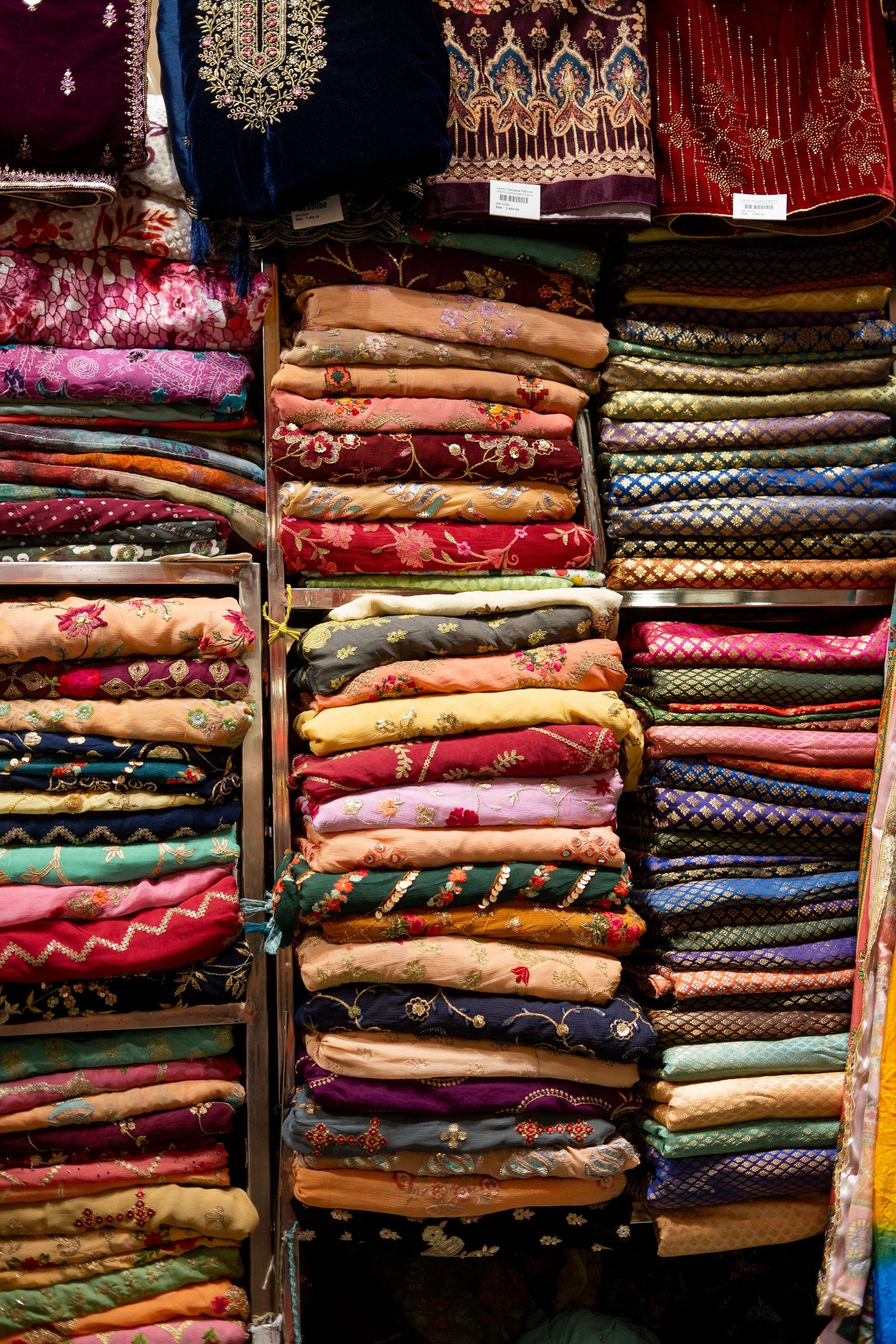 Neatly folded piles of colorful traditional textiles and fabrics arranged on shelves.