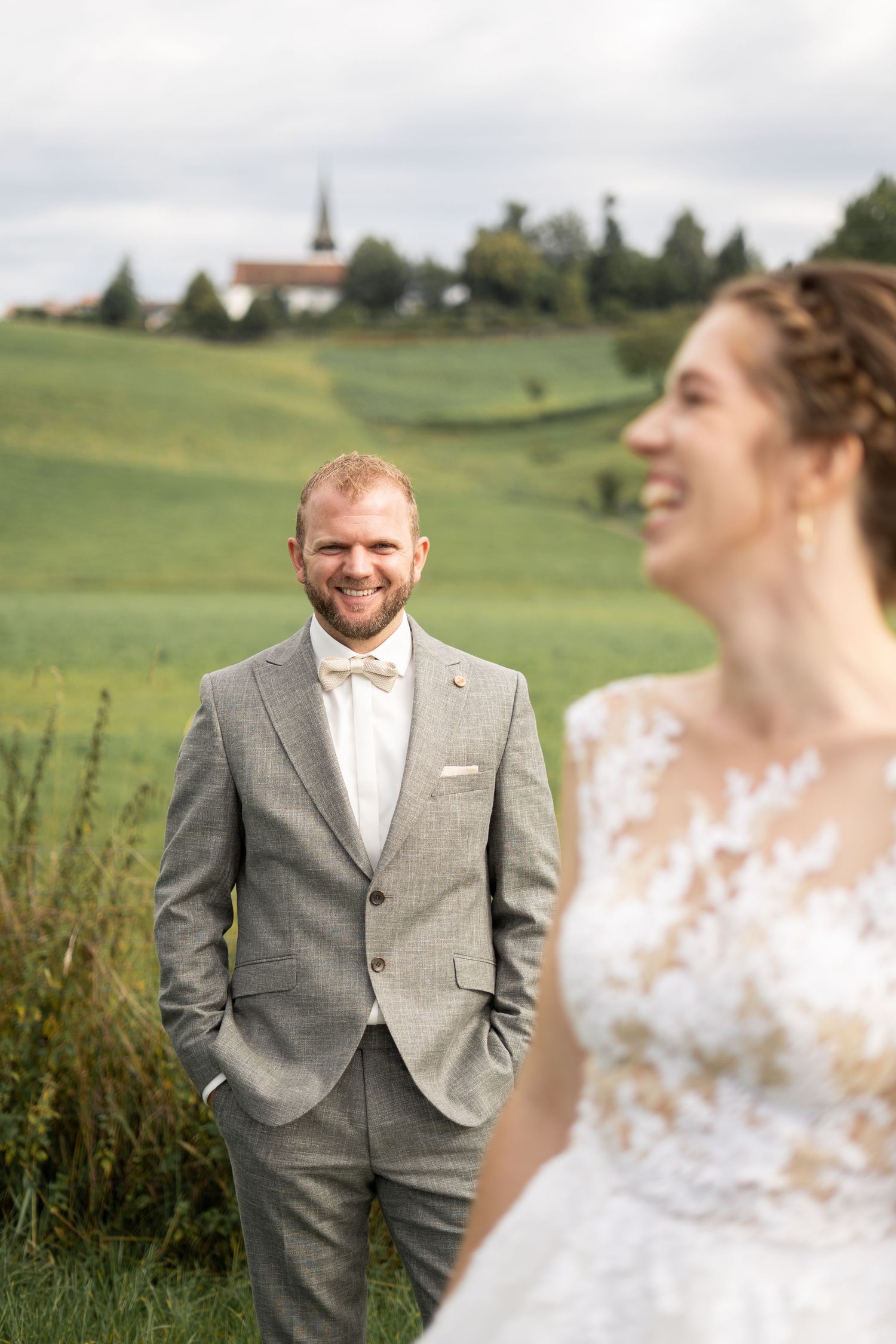 A joyful wedding moment captured in a field with rolling hills and a church in the background.