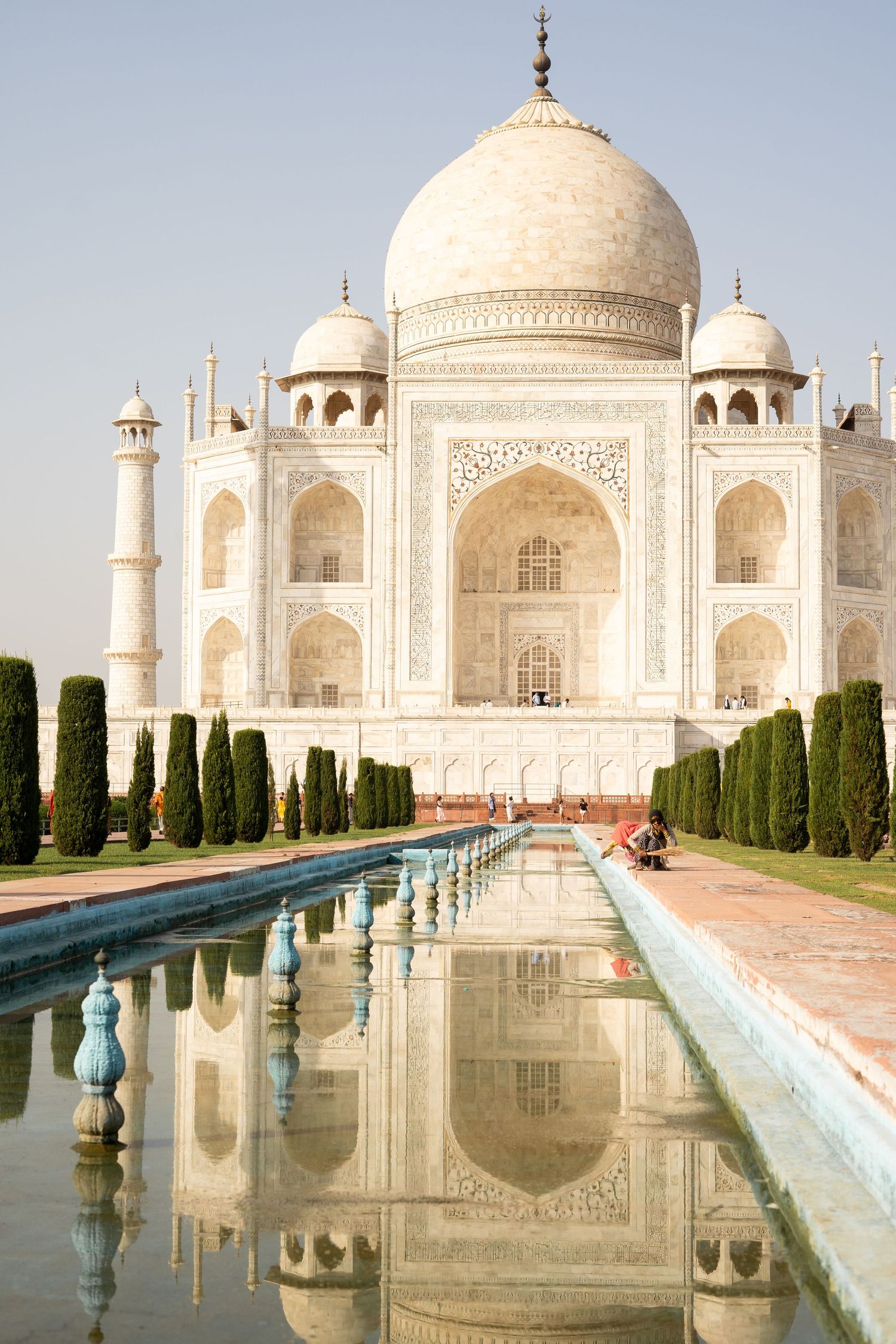Iconic Taj Mahal reflecting in a long water channel lined with cypress trees.