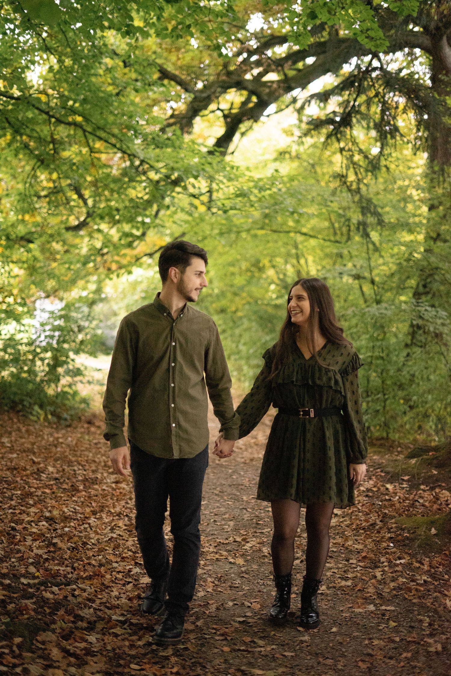 A couple walks hand in hand along a leaf-covered autumn forest path.