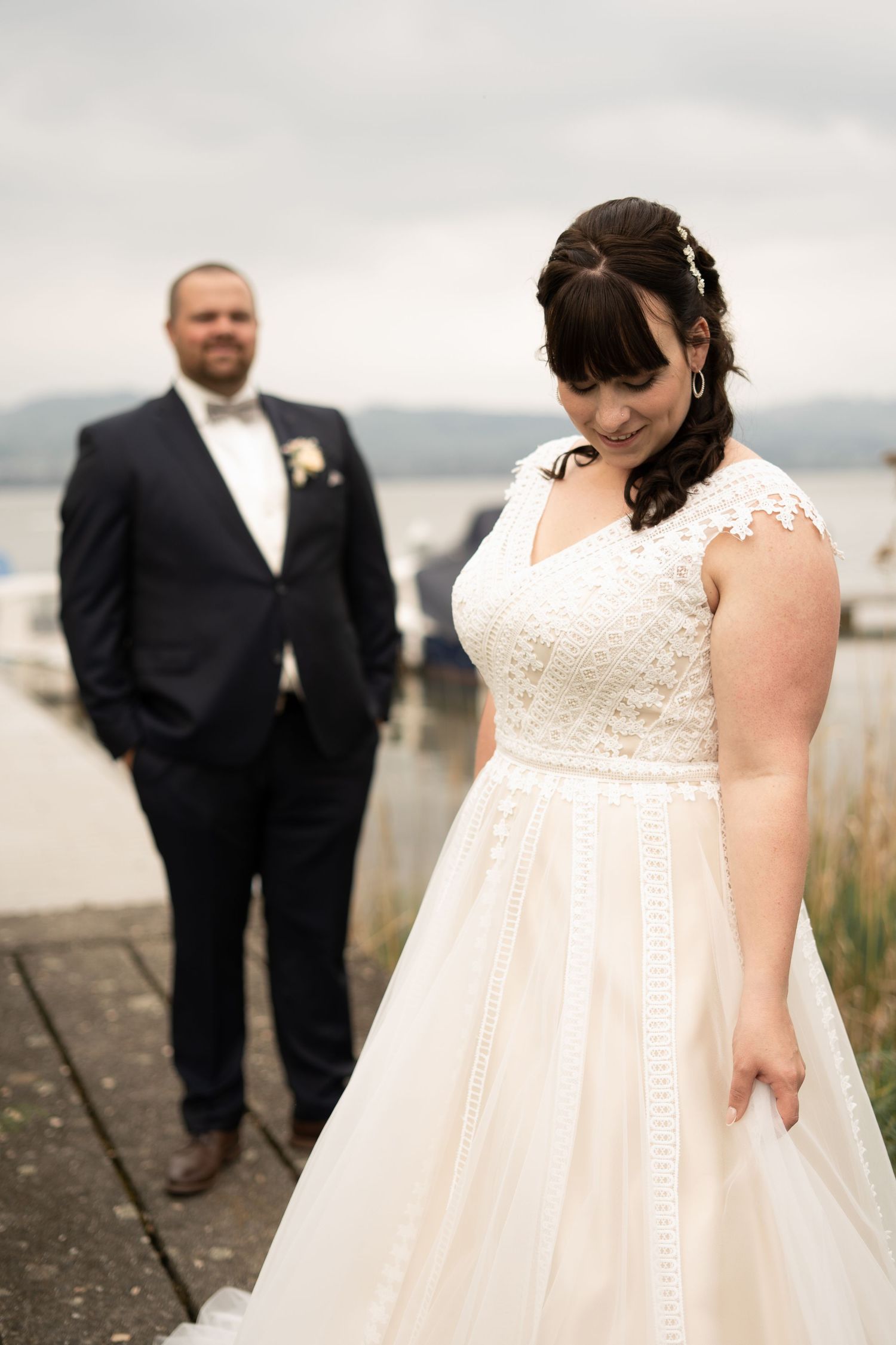 Wedding portraits on a lakefront with overcast skies and boats in the distance.
