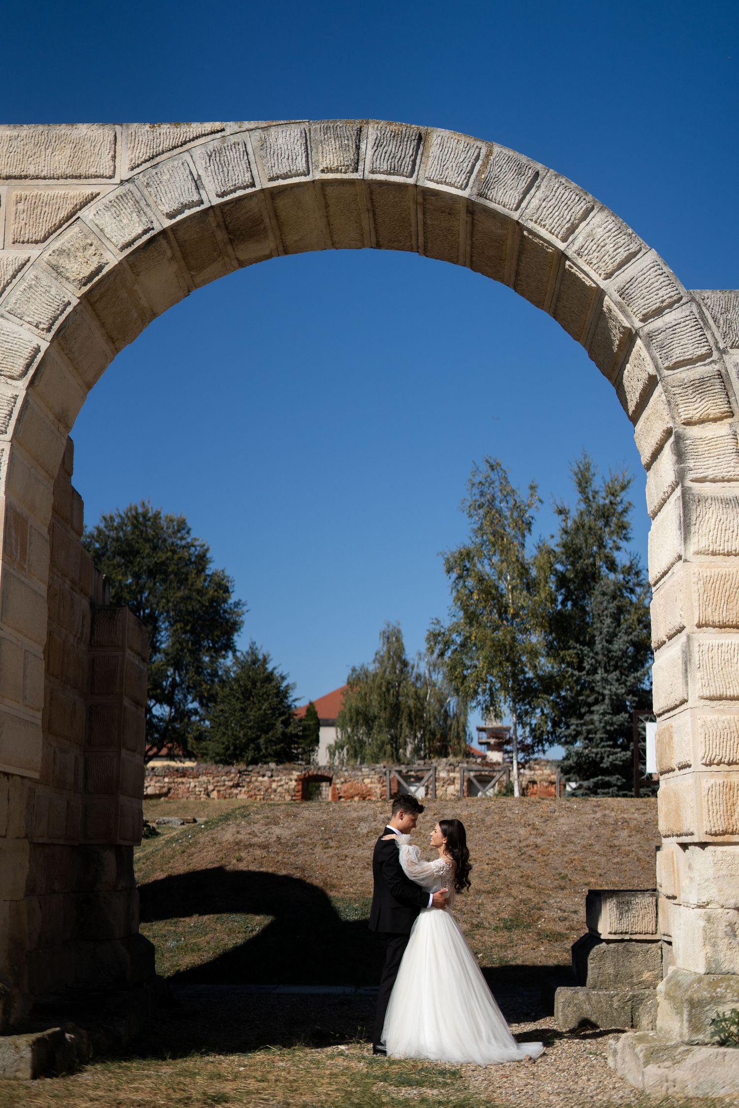 Wedding portraits taken under majestic stone arches against a bright blue sky.