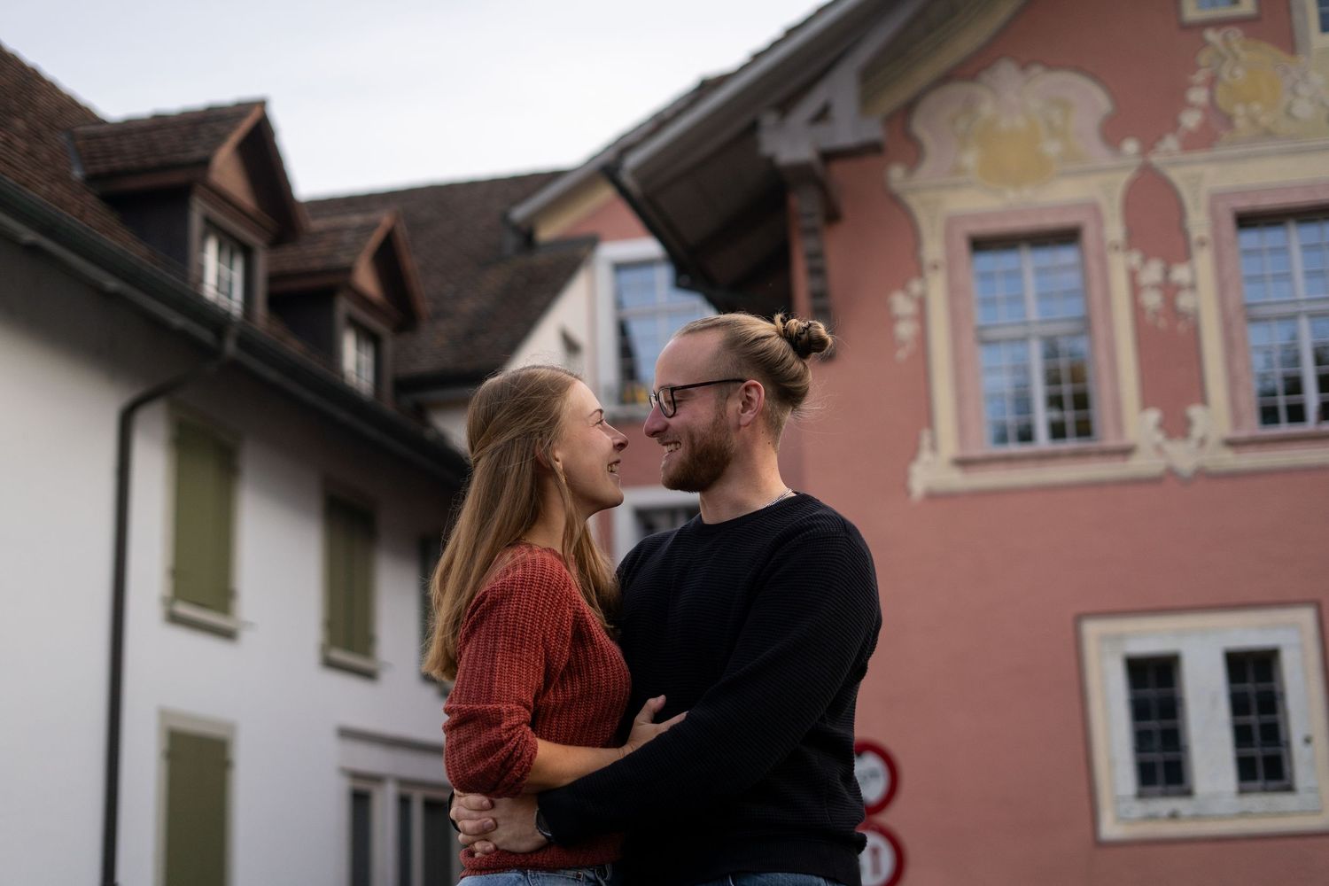 Couple poses in front of pink traditional European buildings during engagement session.