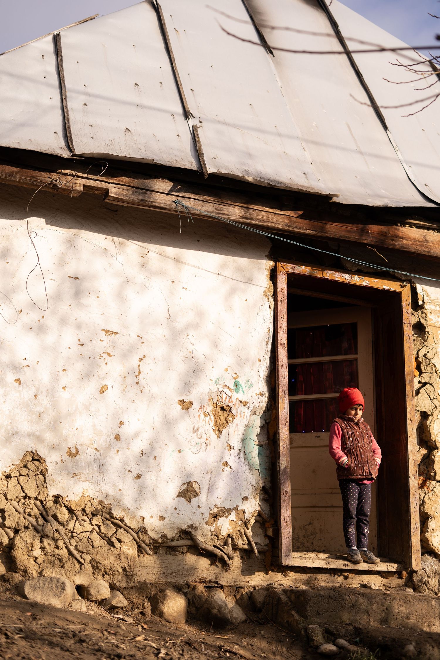 A small figure stands in the doorway of a weathered white stucco building.