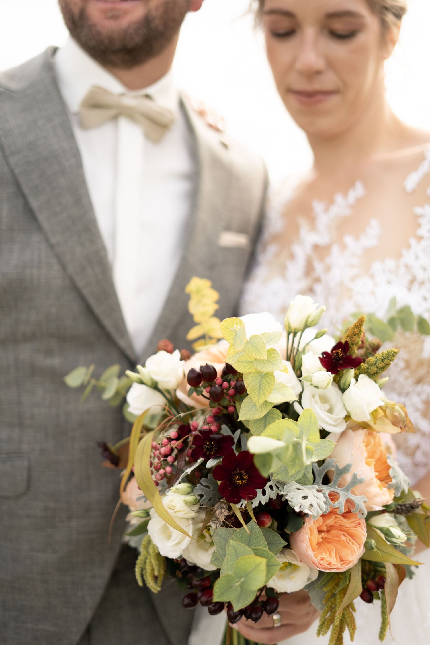 A stunning wedding bouquet featuring burgundy and peach flowers with delicate lace details.