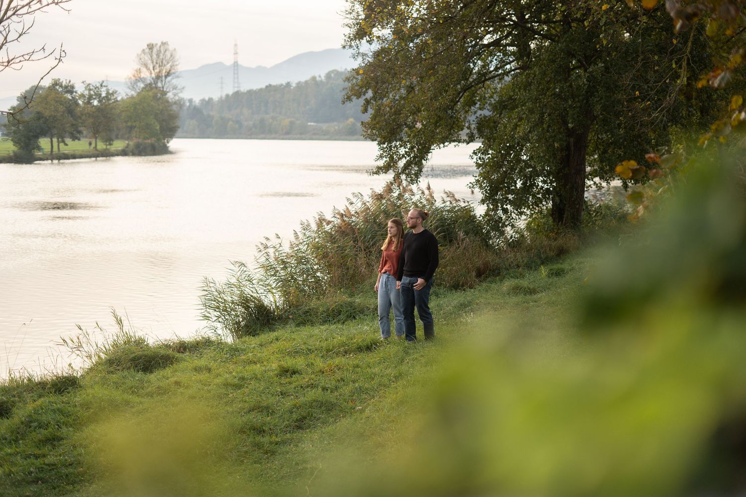 Silhouetted couple stands together on grassy hillside during golden hour.