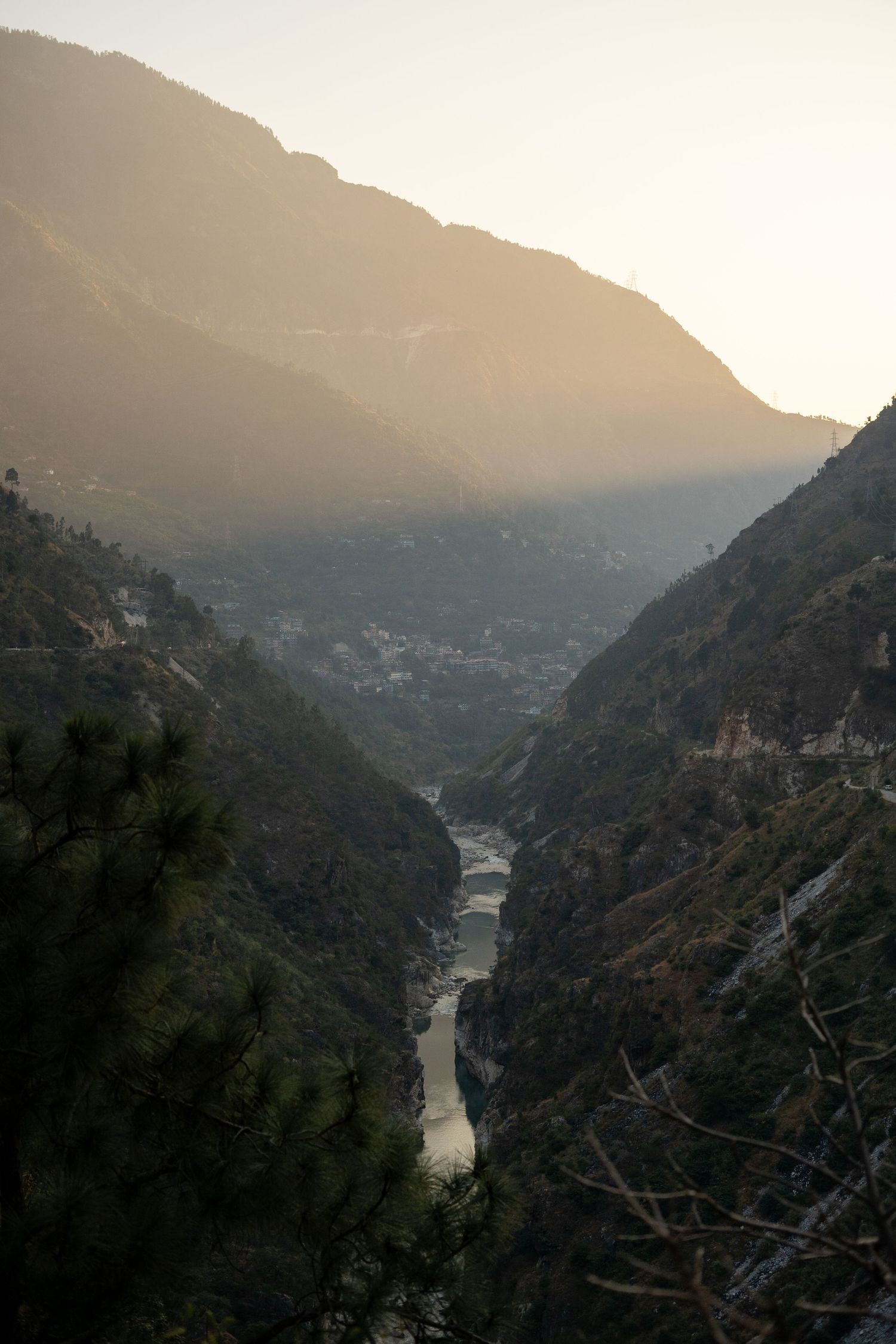 A dramatic mountain valley with a winding river below captured during golden hour in misty conditions.