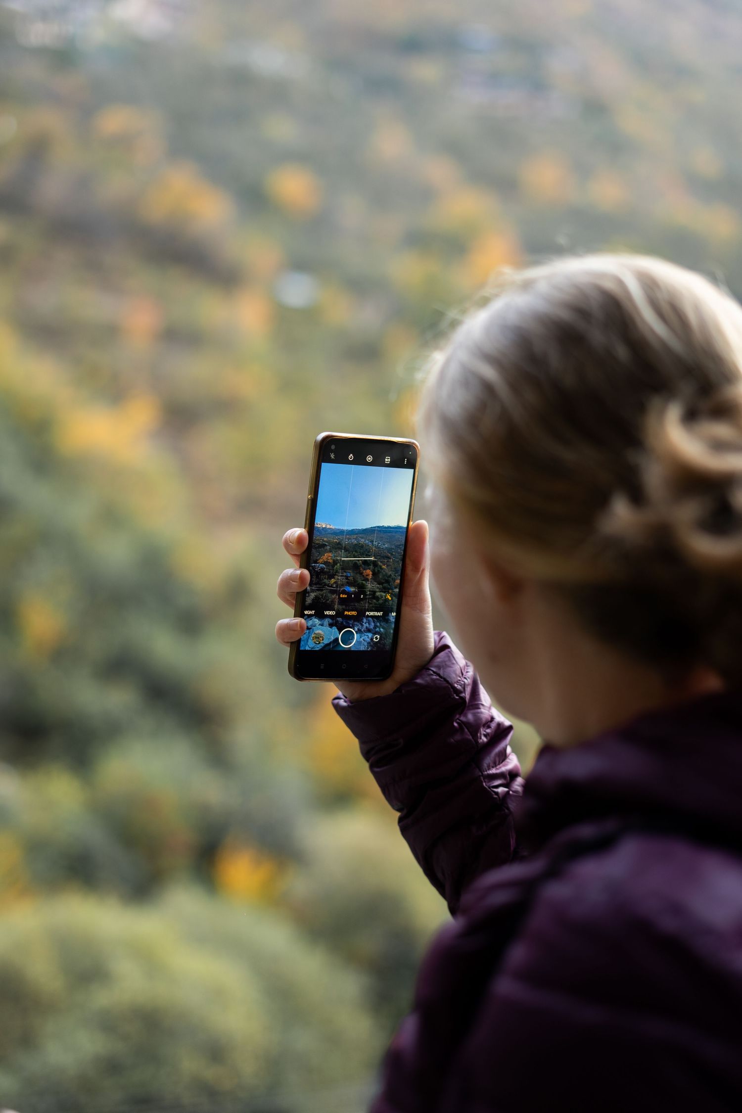 Someone taking a photo of mountain scenery with a smartphone against an autumn landscape.