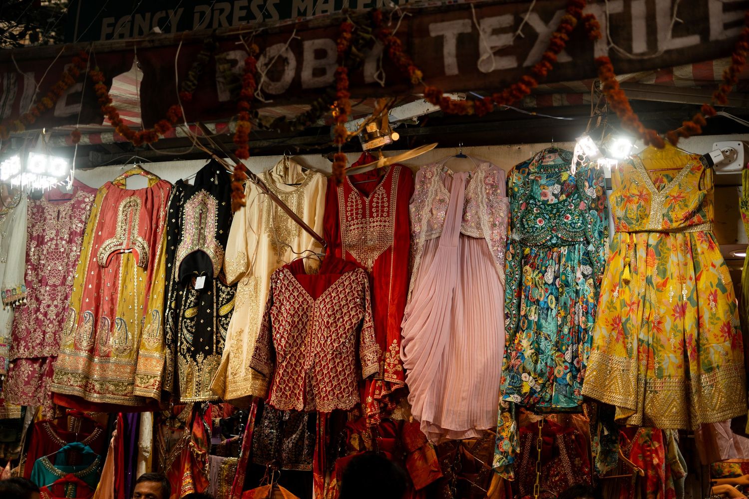 Rows of colorful dresses and textiles hanging in a covered market.