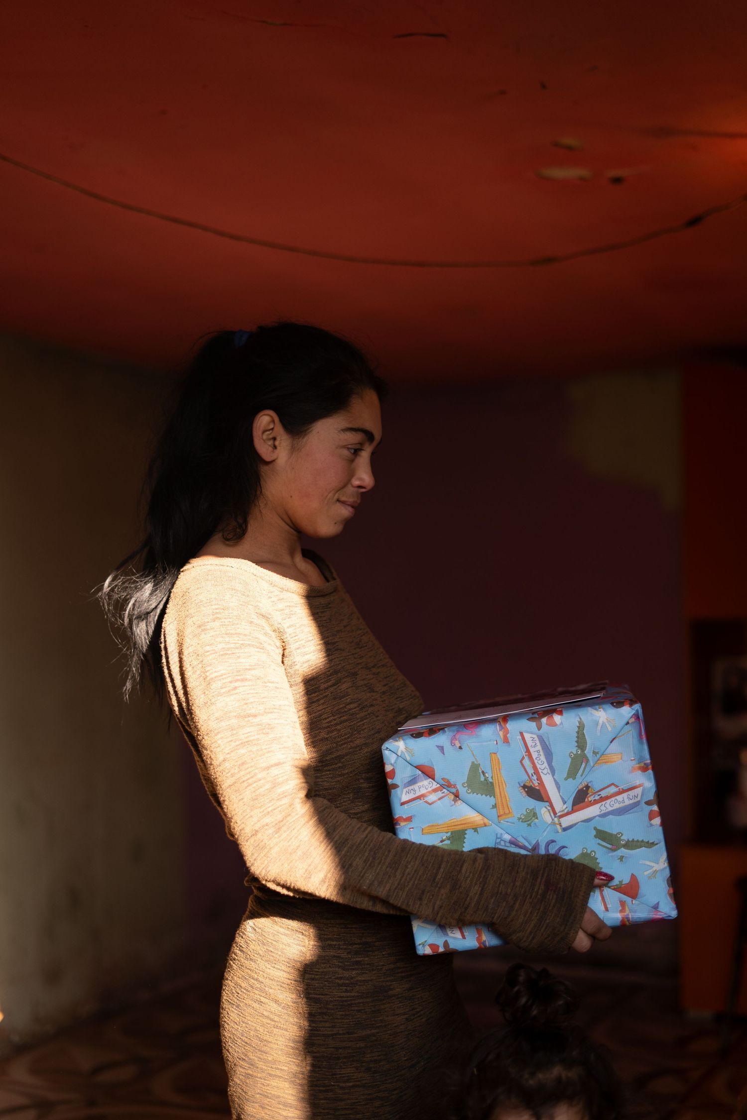 A person in a cream sweater holds a wrapped gift in a dimly lit room.