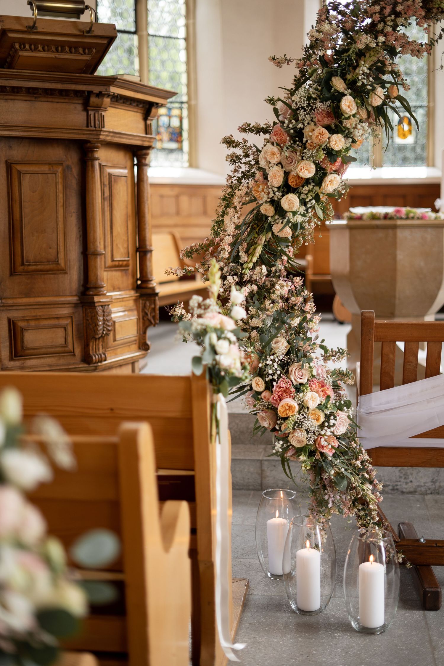 Elegant floral arrangement with pink roses cascading down a wooden church pulpit with candles below.