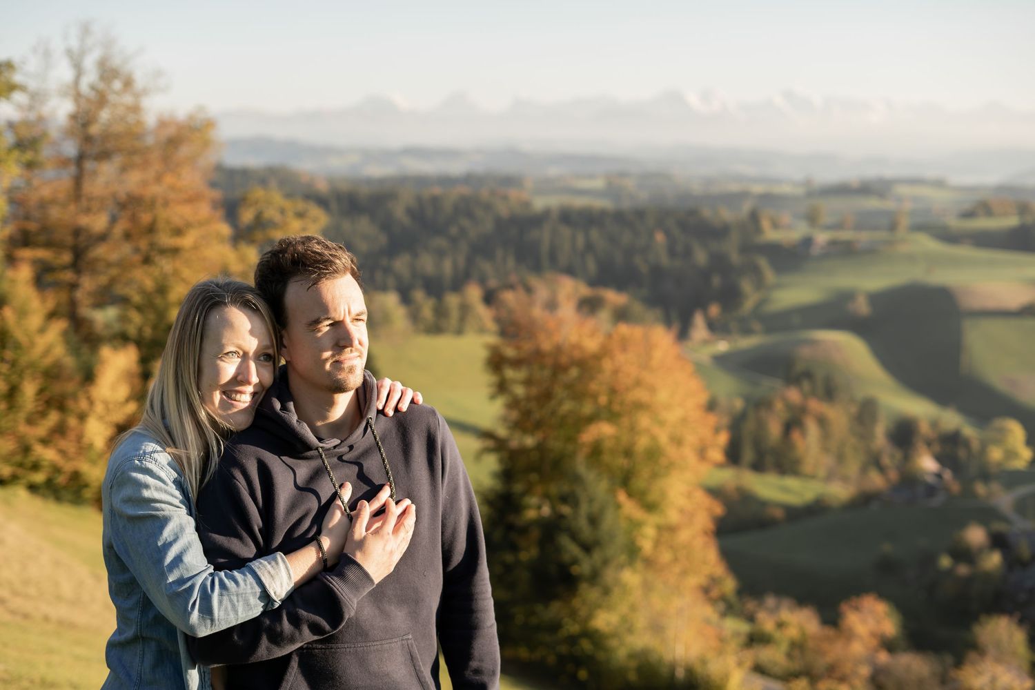 A couple shares an intimate moment on a hilltop against a backdrop of rolling countryside.